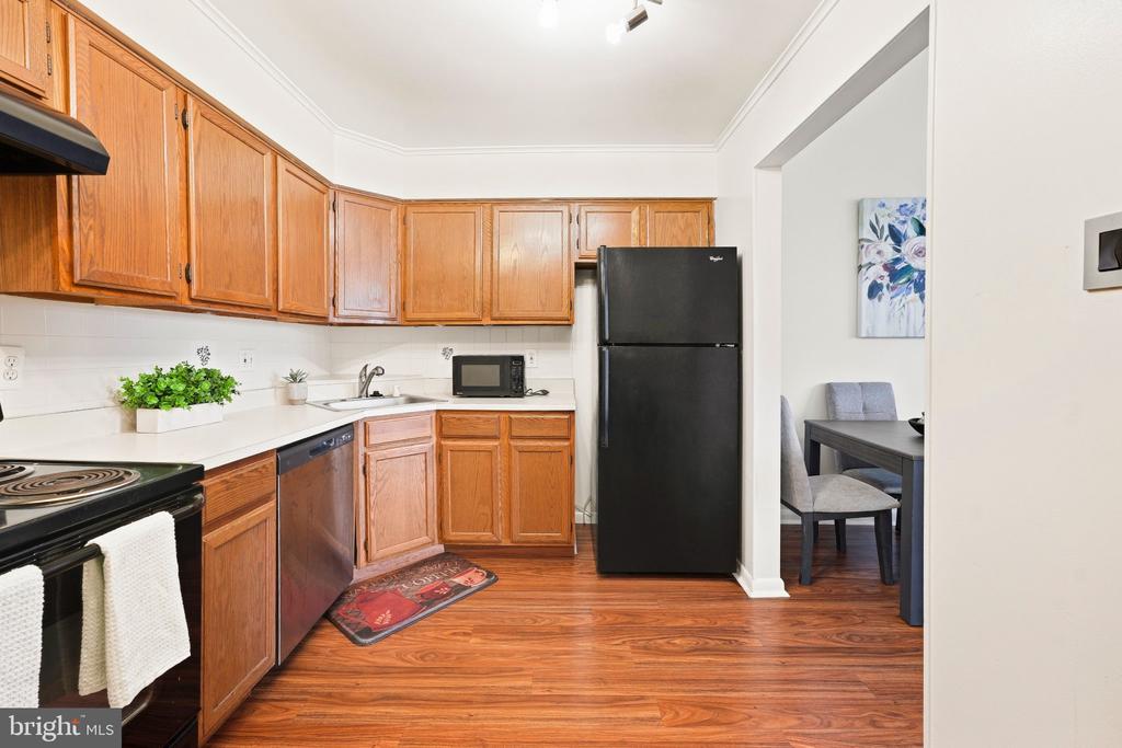 Kitchen with wood cabinets, white counters, black appliances, and an adjoining dining area.