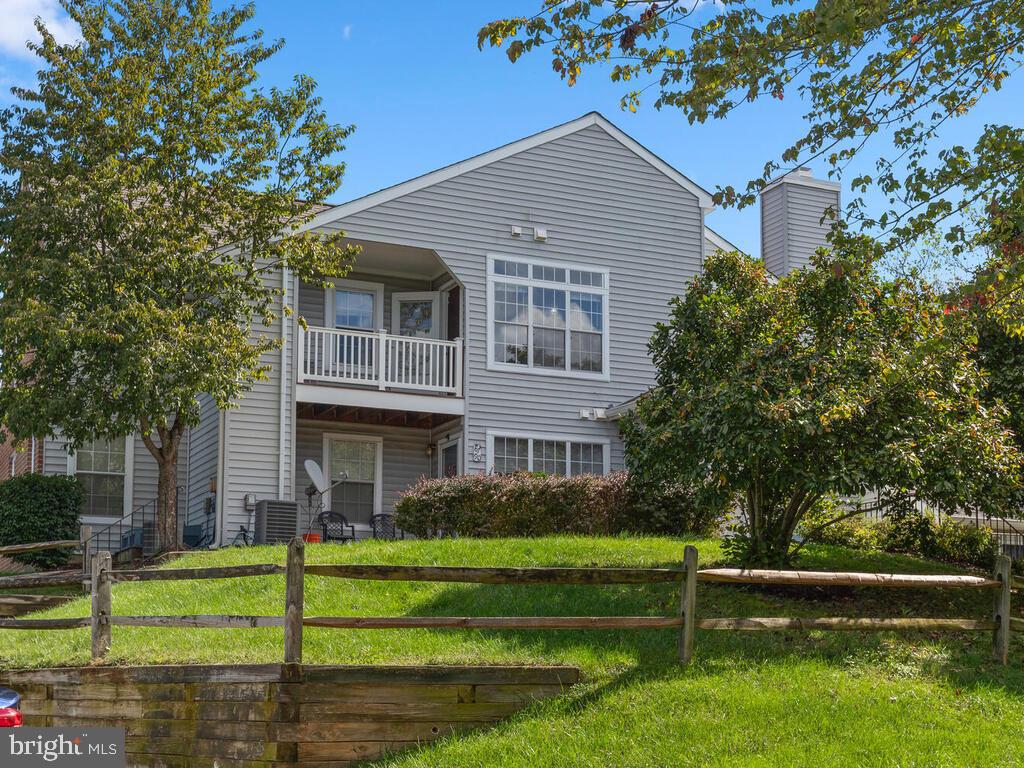 Gray two-story home with a second-floor balcony and fenced grassy yard.
