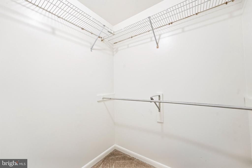 Empty walk-in closet with white wire shelving, a hanging rod, and beige carpet.