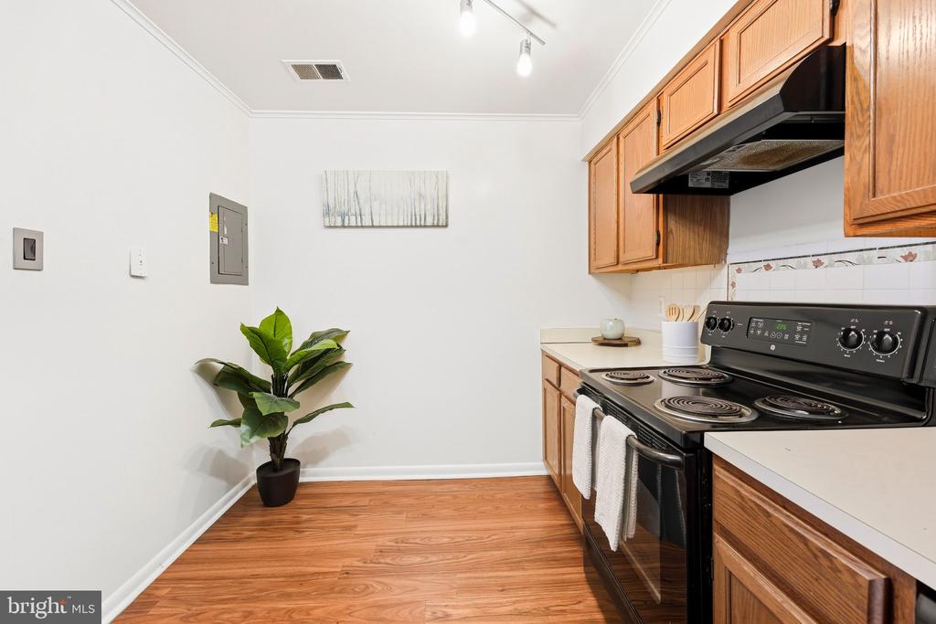 Kitchen with honey-colored cabinets, a black electric range, and wood-look flooring.