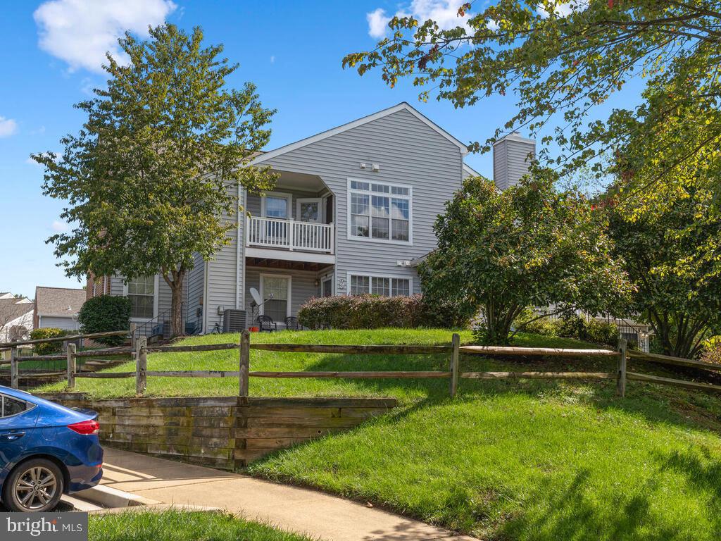 Two-story gray-sided home with a balcony, leafy trees, and a split-rail fence.