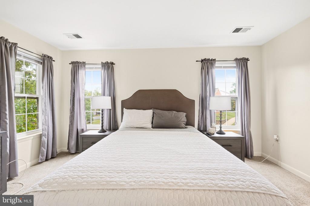 Furnished bedroom with a white-quilted bed, brown headboard, gray curtains, and three windows.