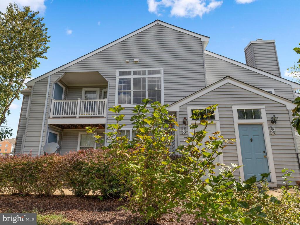 Gray-sided home with a covered balcony, light blue front door, and landscaped shrubs.