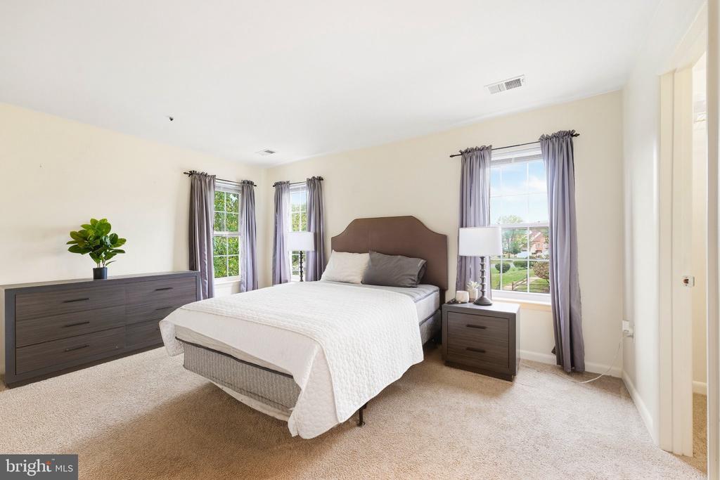 Bedroom with a white-covered bed, dark wood furniture, beige carpet, and three curtained windows.