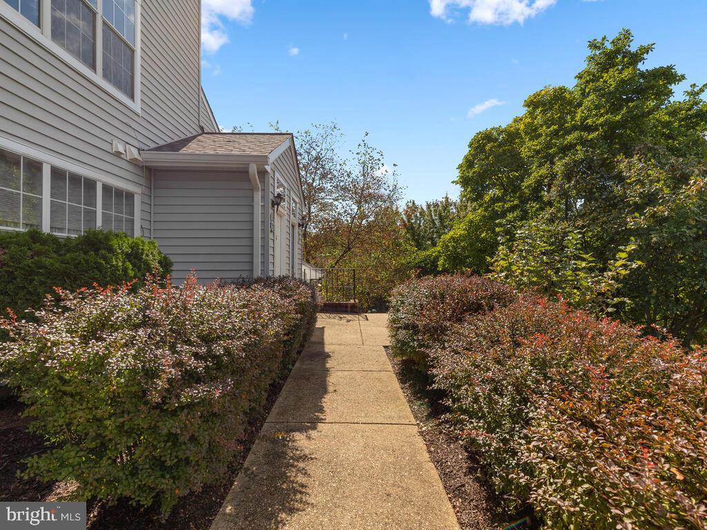 Gray-sided home beside a concrete walkway bordered by shrubs and trees.