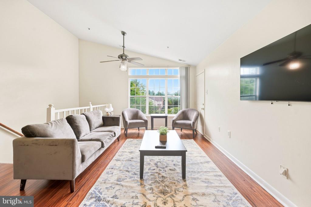 Living room with a gray sofa, armchairs, wall-mounted TV, and large window overlooking greenery.