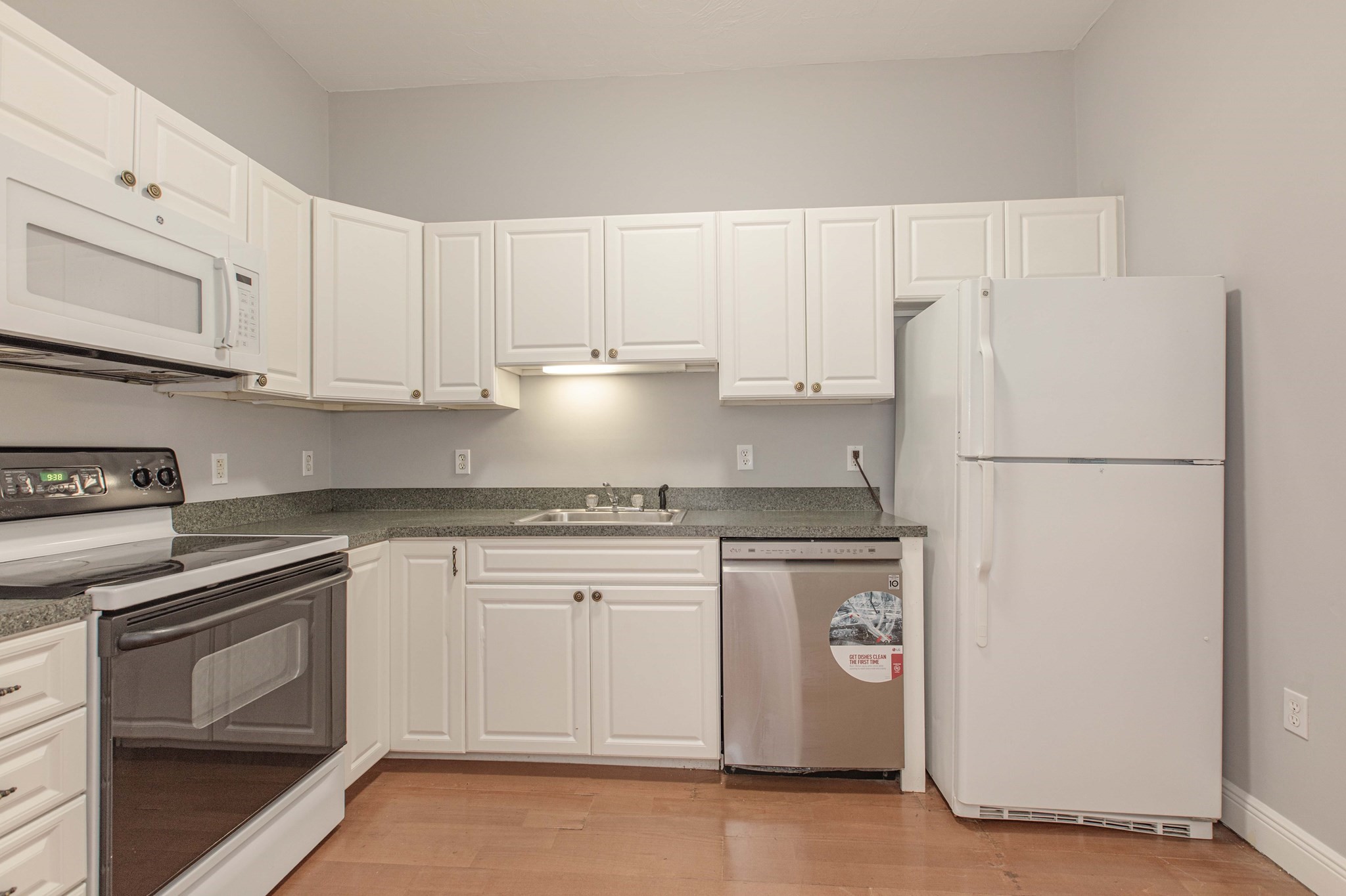 Kitchen with white cabinets, gray-speckled counters, stainless dishwasher, and hardwood flooring.