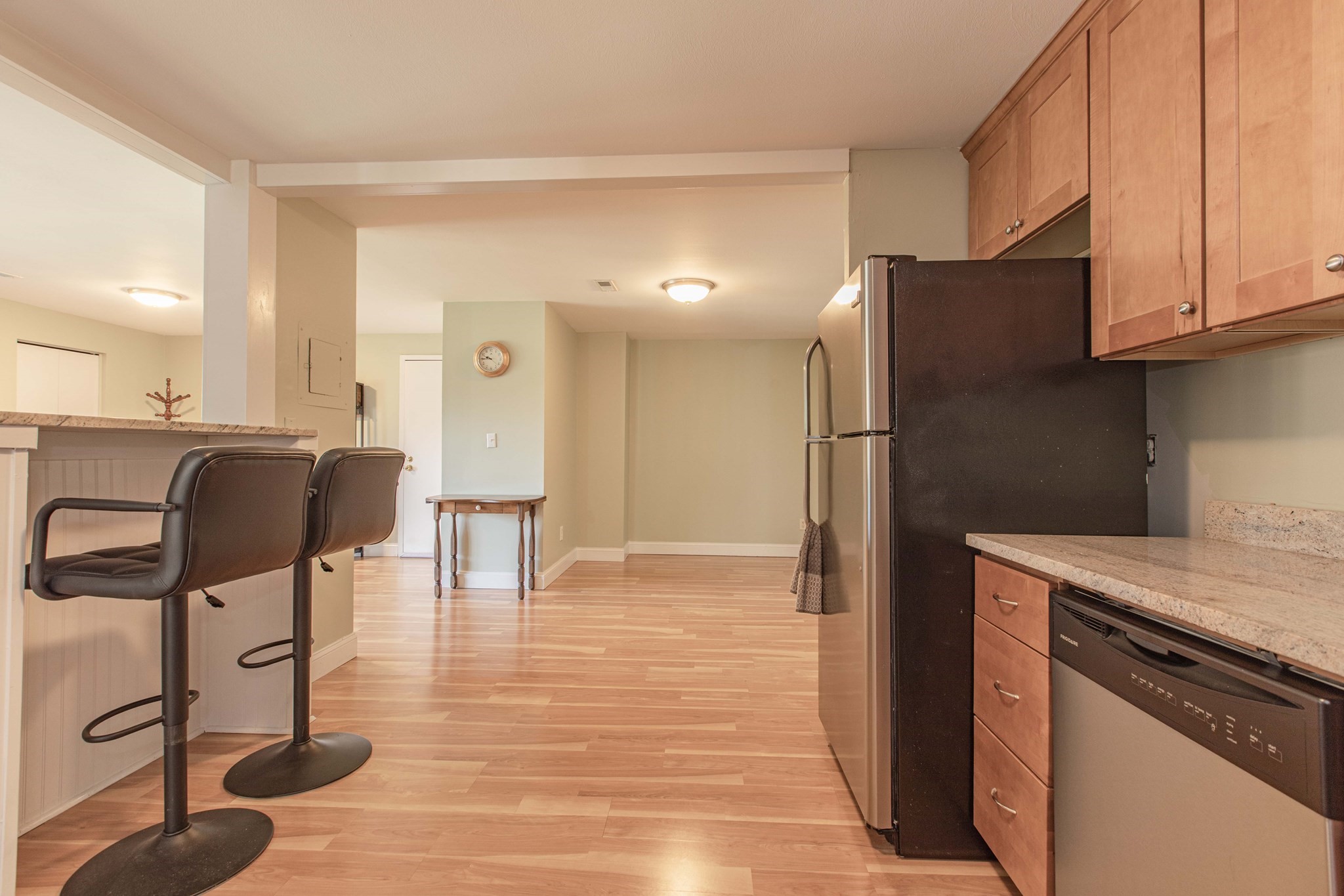 Kitchen with wood cabinets, granite counters, a dark refrigerator, and a breakfast bar with two stools.