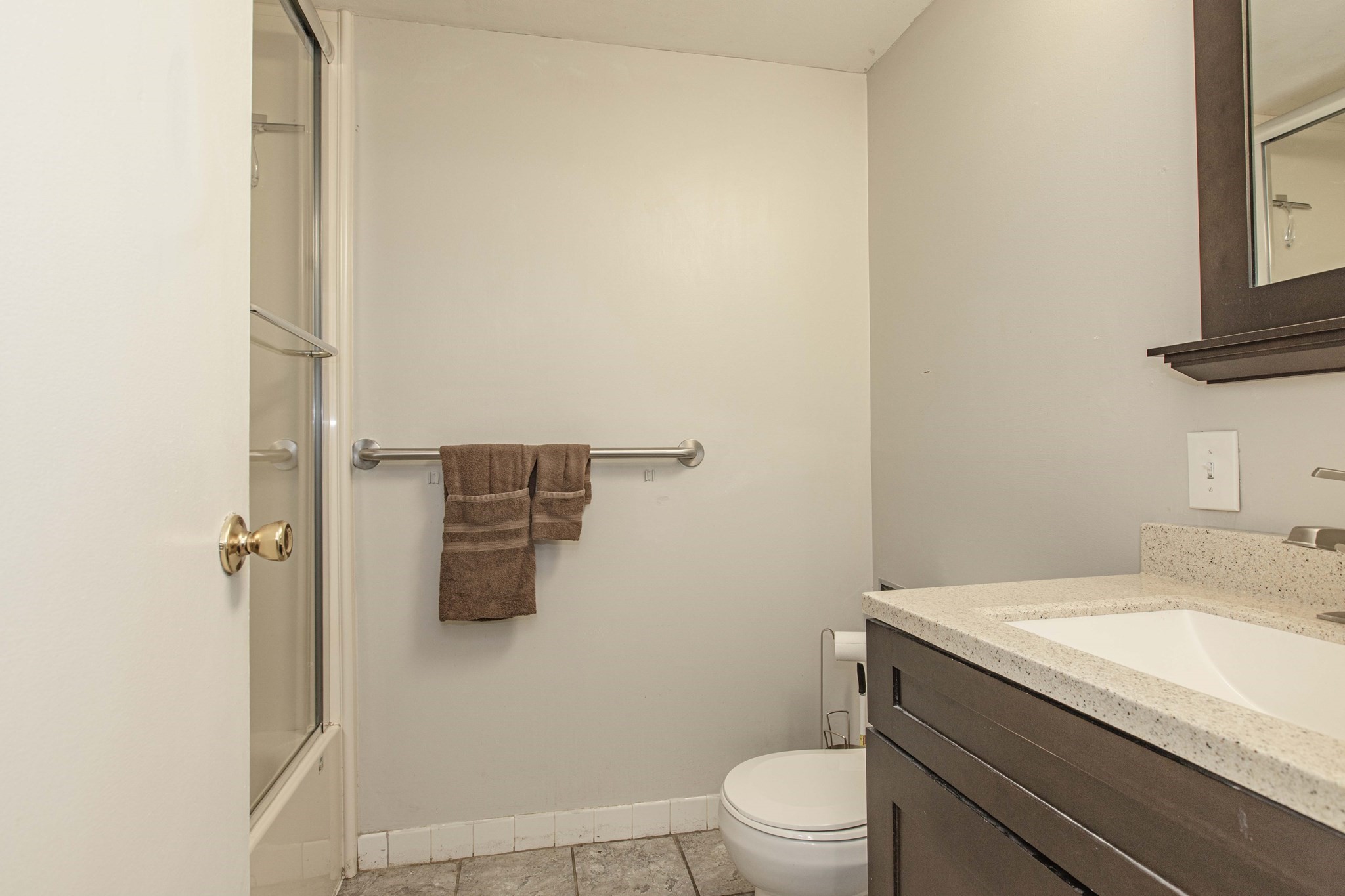 Bathroom with glass shower, dark wood vanity, and brown towels on a wall-mounted bar.