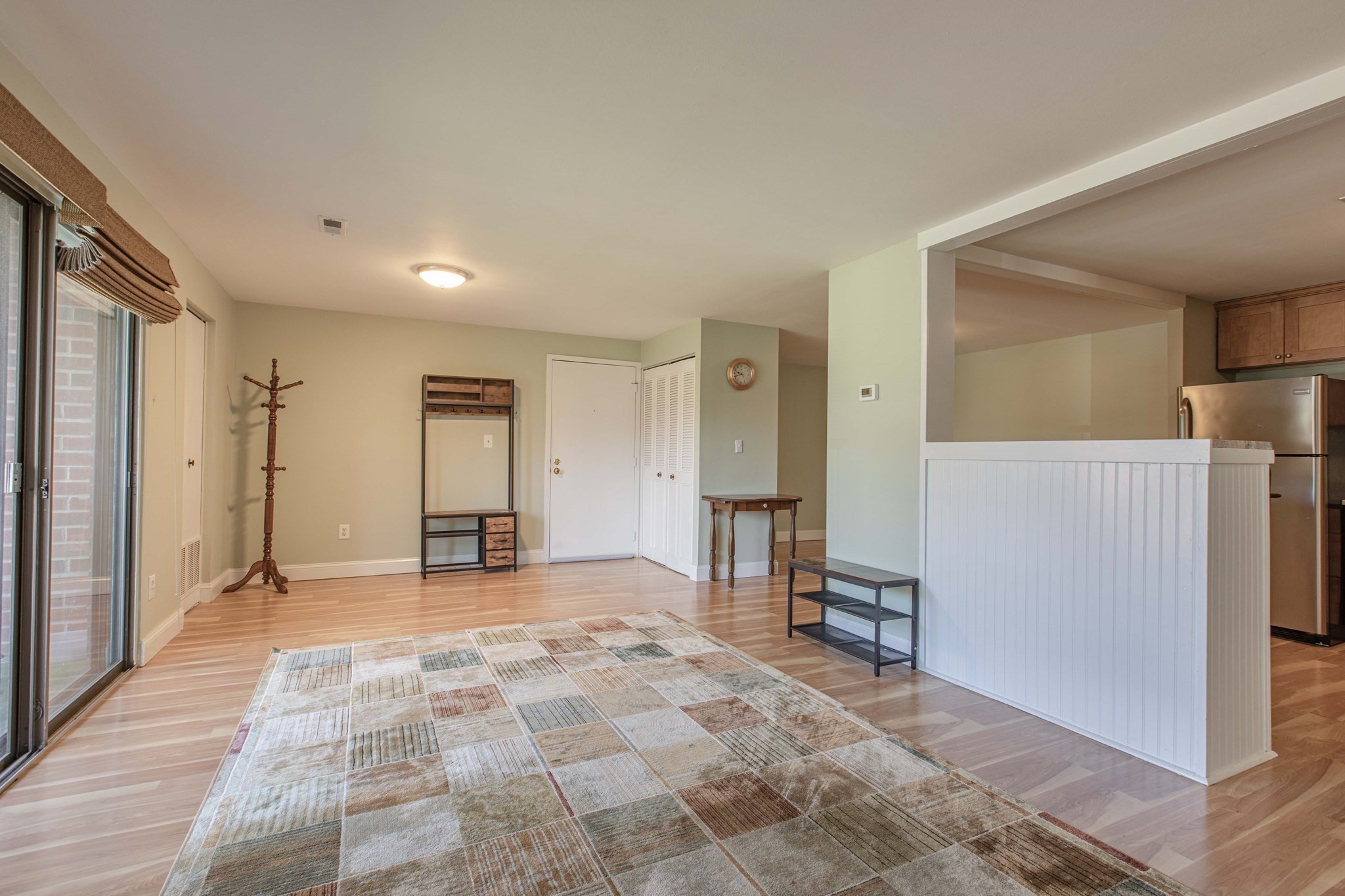 Living area with light wood floors and a patchwork rug, opening to a kitchen with a breakfast counter.