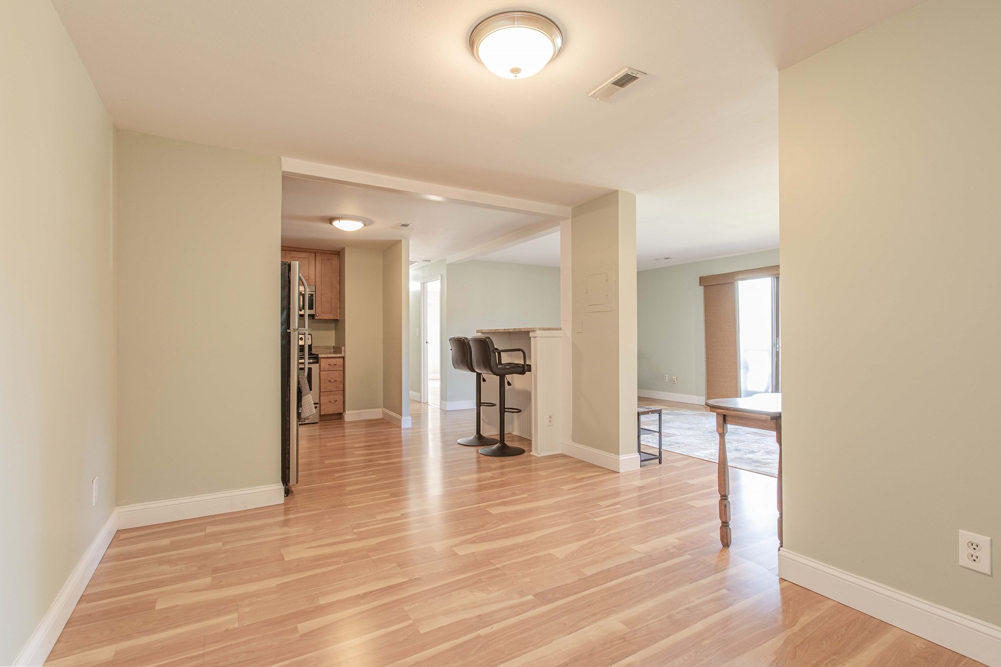 Open-plan condo living area with wood floors, kitchen bar, and two stools.