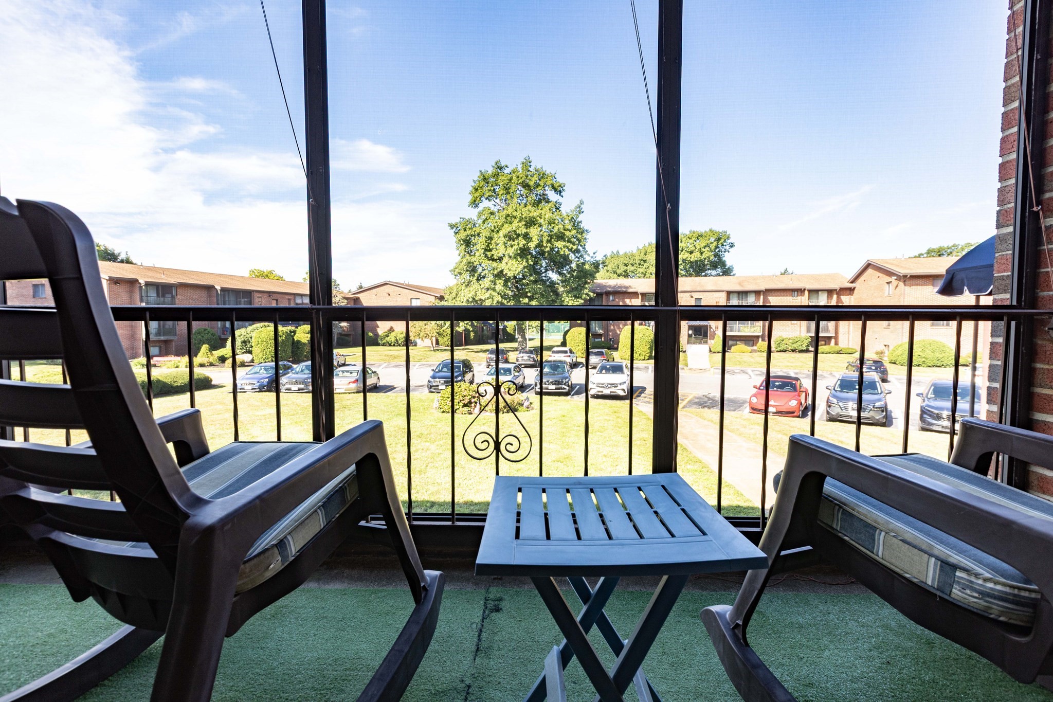 Furnished apartment balcony with outdoor seating overlooking a landscaped courtyard and parking area.