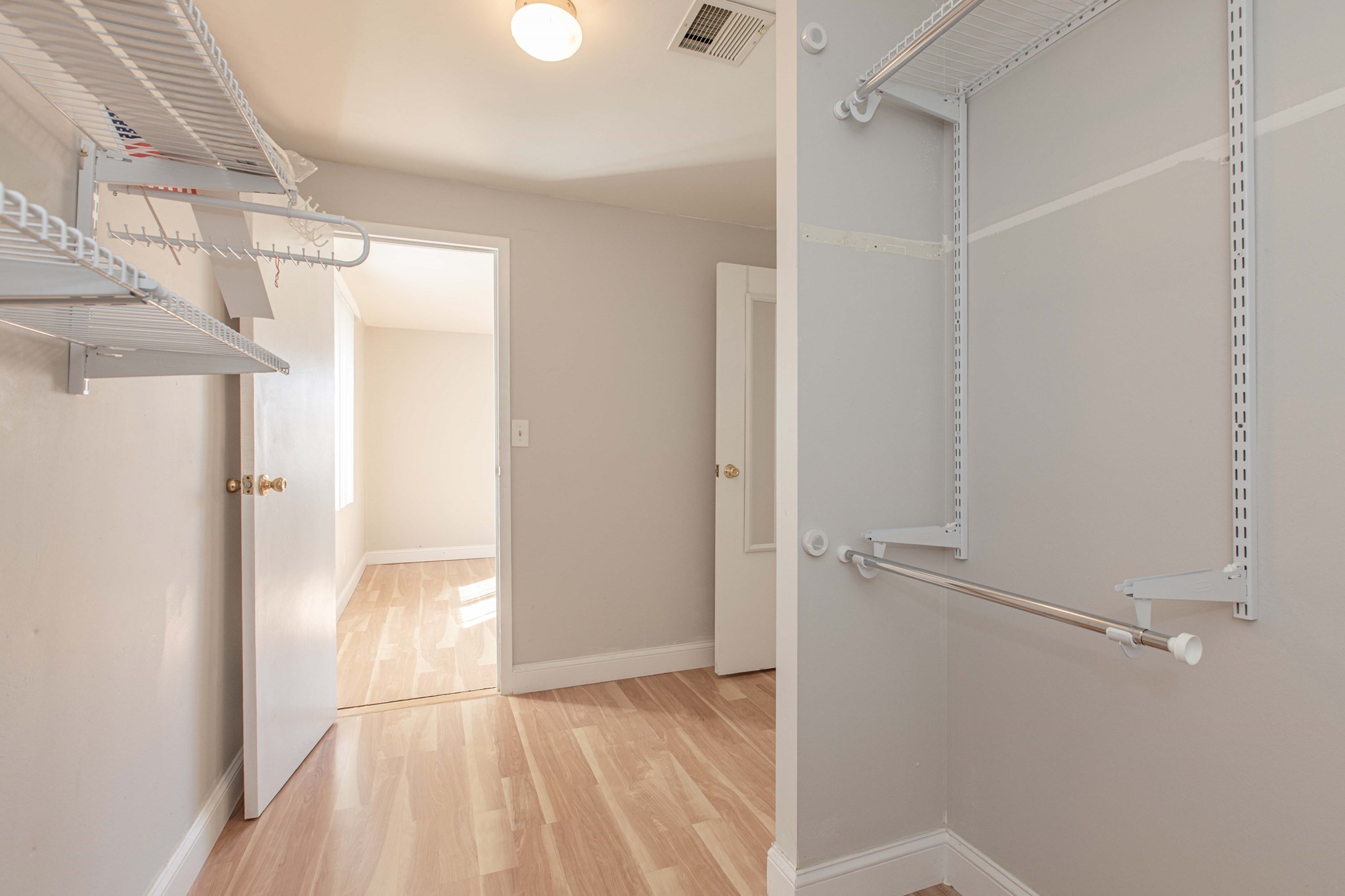 Walk-in closet with wire shelving, adjustable clothes rails, and light wood flooring.