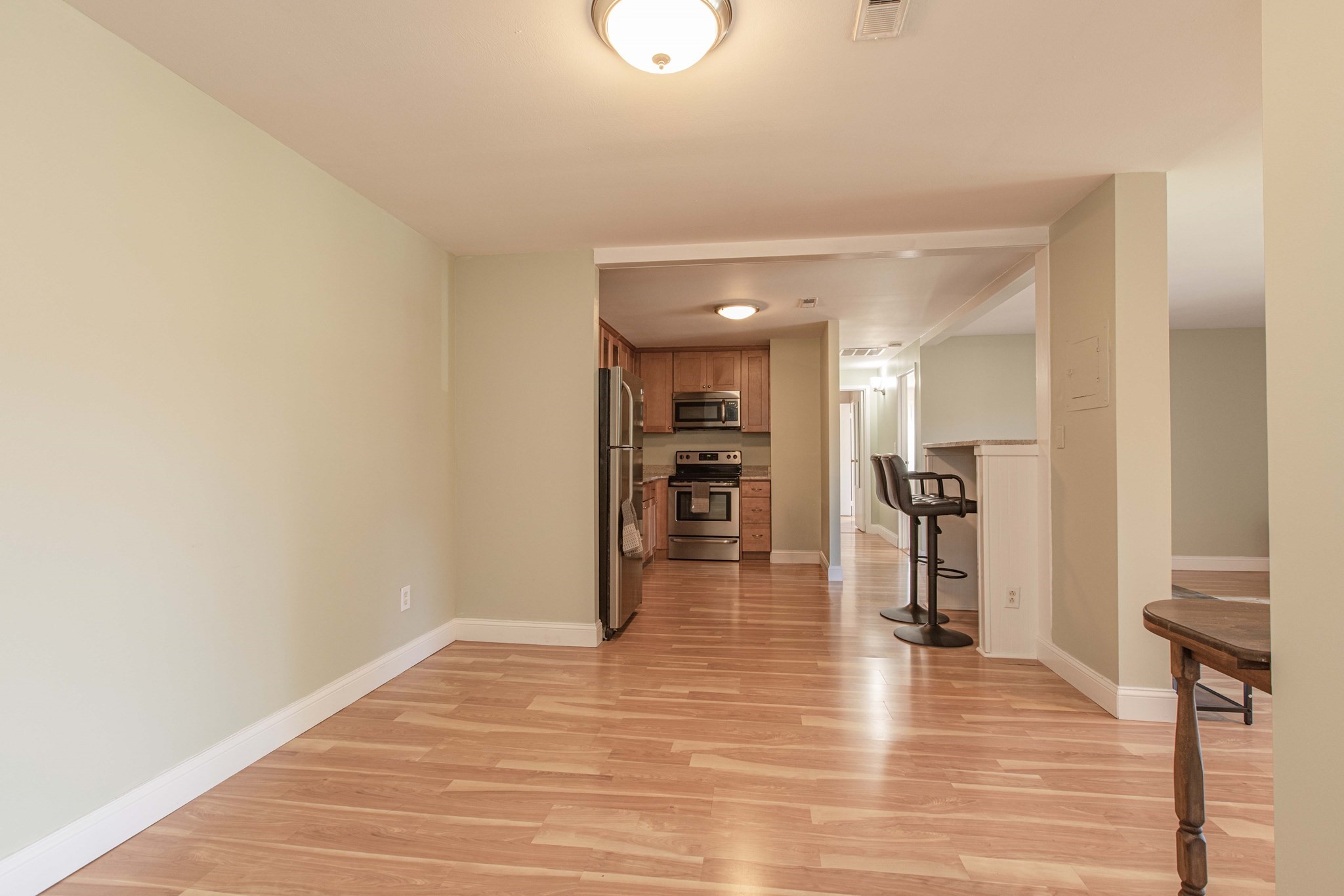 Open-plan condo kitchen with wood cabinets, stainless steel appliances, breakfast bar, and hardwood floors.