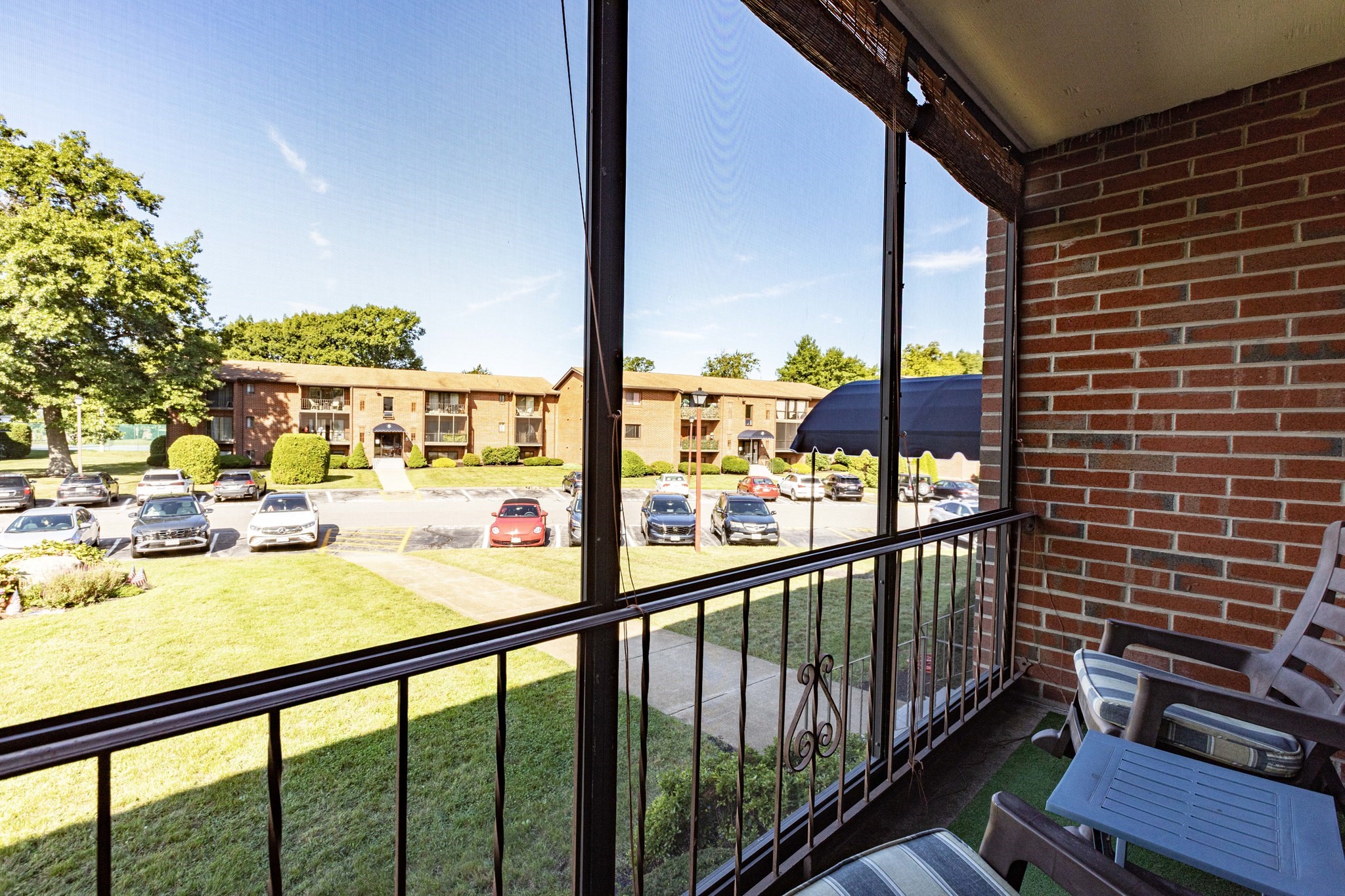 Furnished balcony overlooking a lawn, parking lot, and brick apartment building.