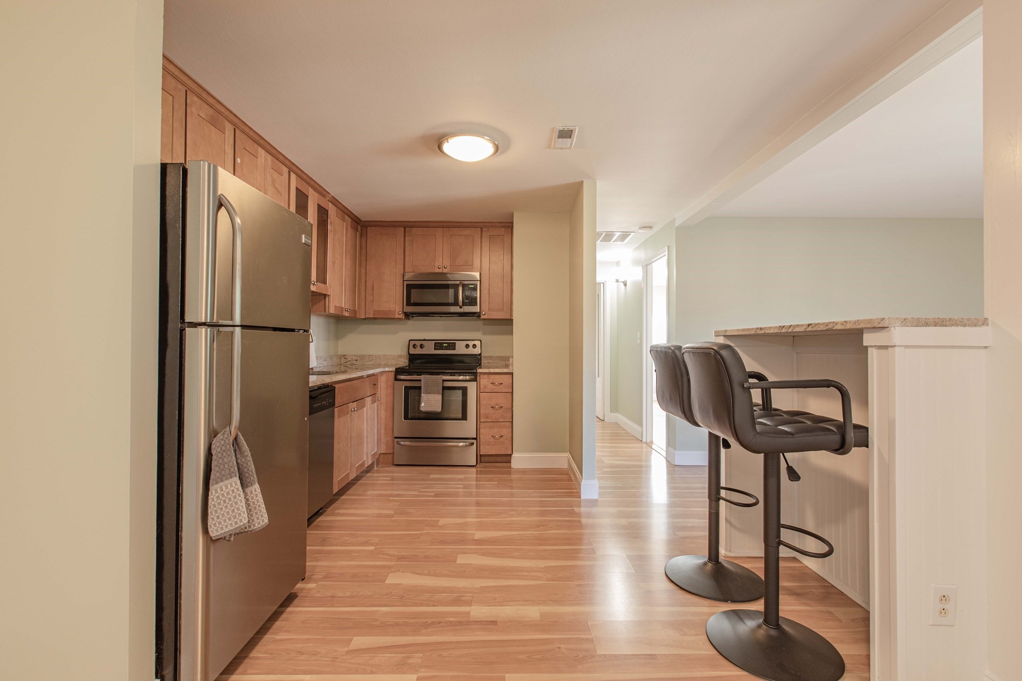 Kitchen with wood cabinets and stainless appliances beside a breakfast bar with two stools.