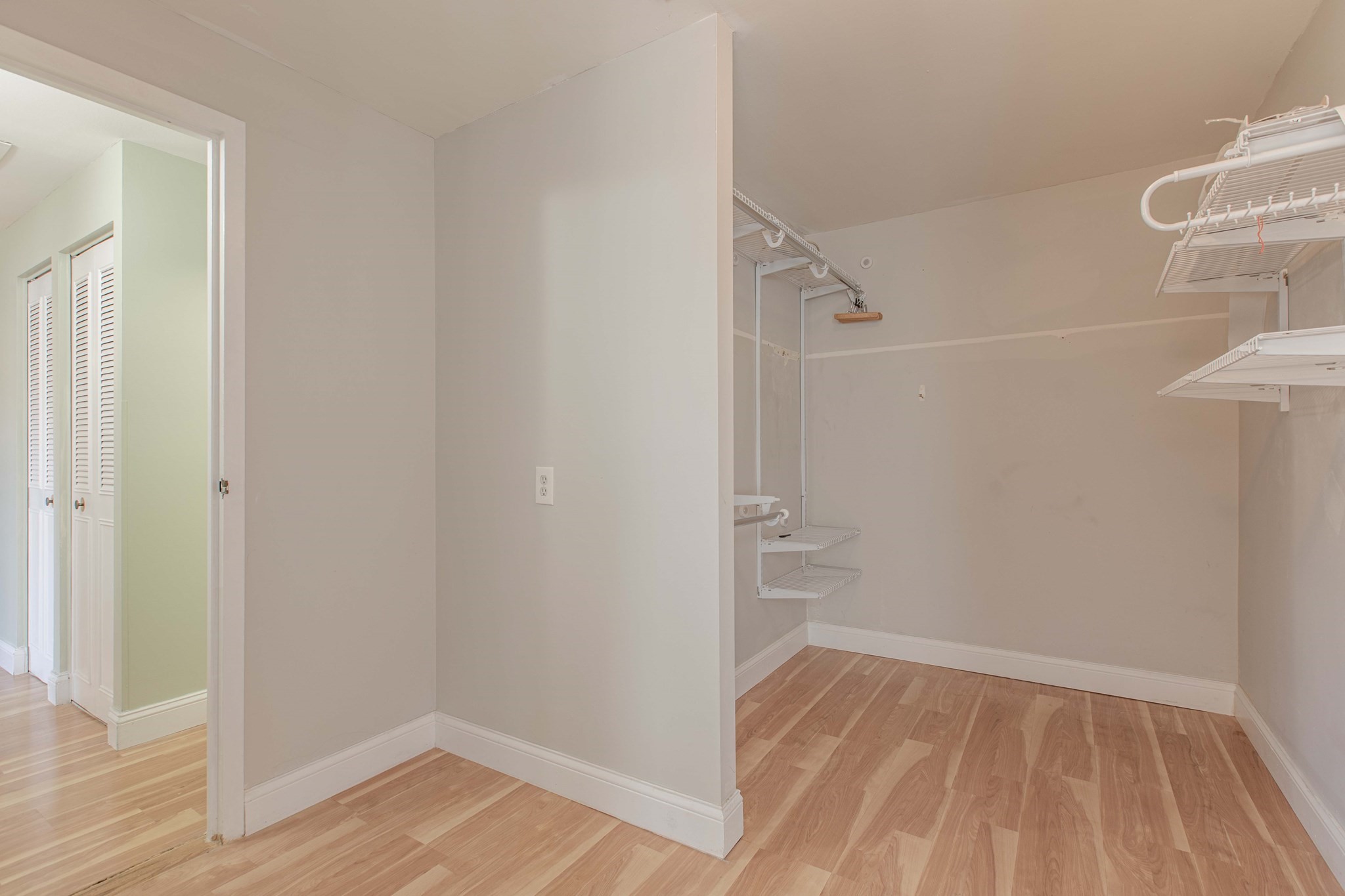 Empty walk-in closet with wood flooring and white wire shelving.