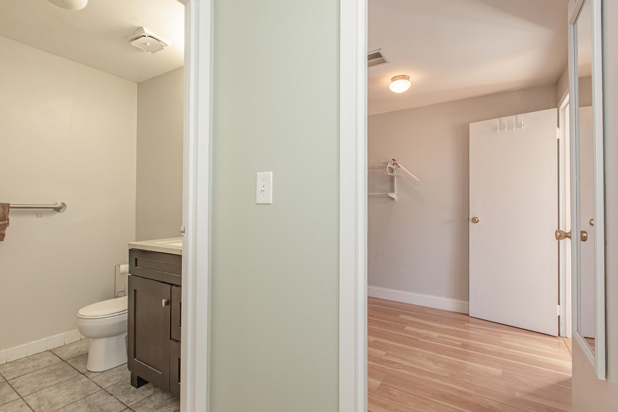 Bathroom with dark vanity and tiled floor beside a walk-in closet with mirrored doors.