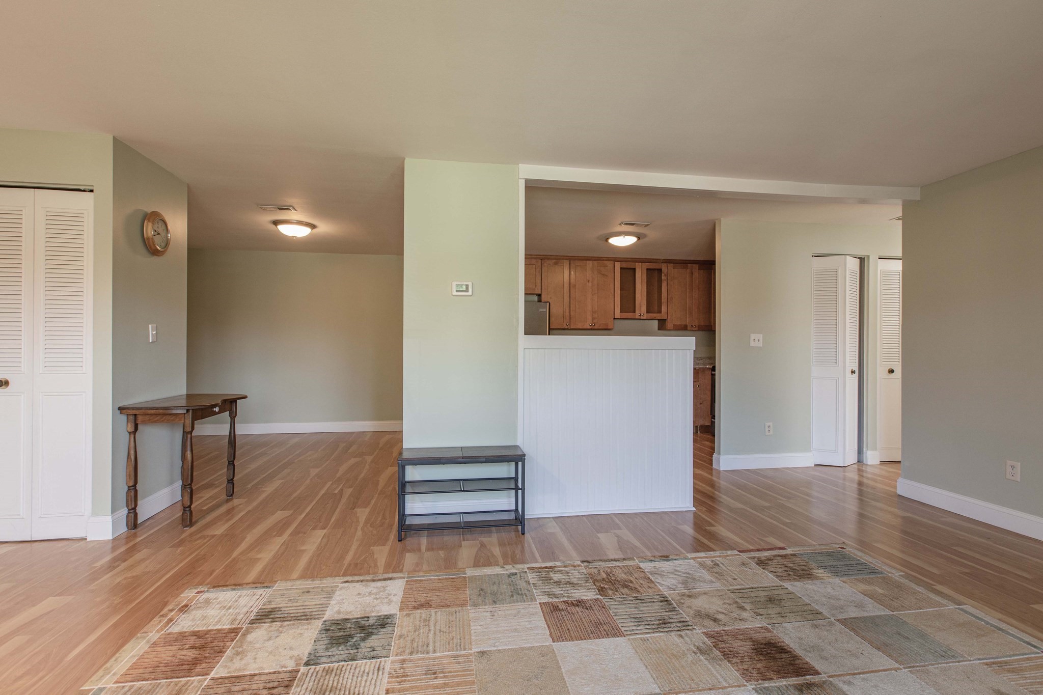 Open-plan living area with wood floors, a patchwork rug, and a kitchen behind a half-wall.
