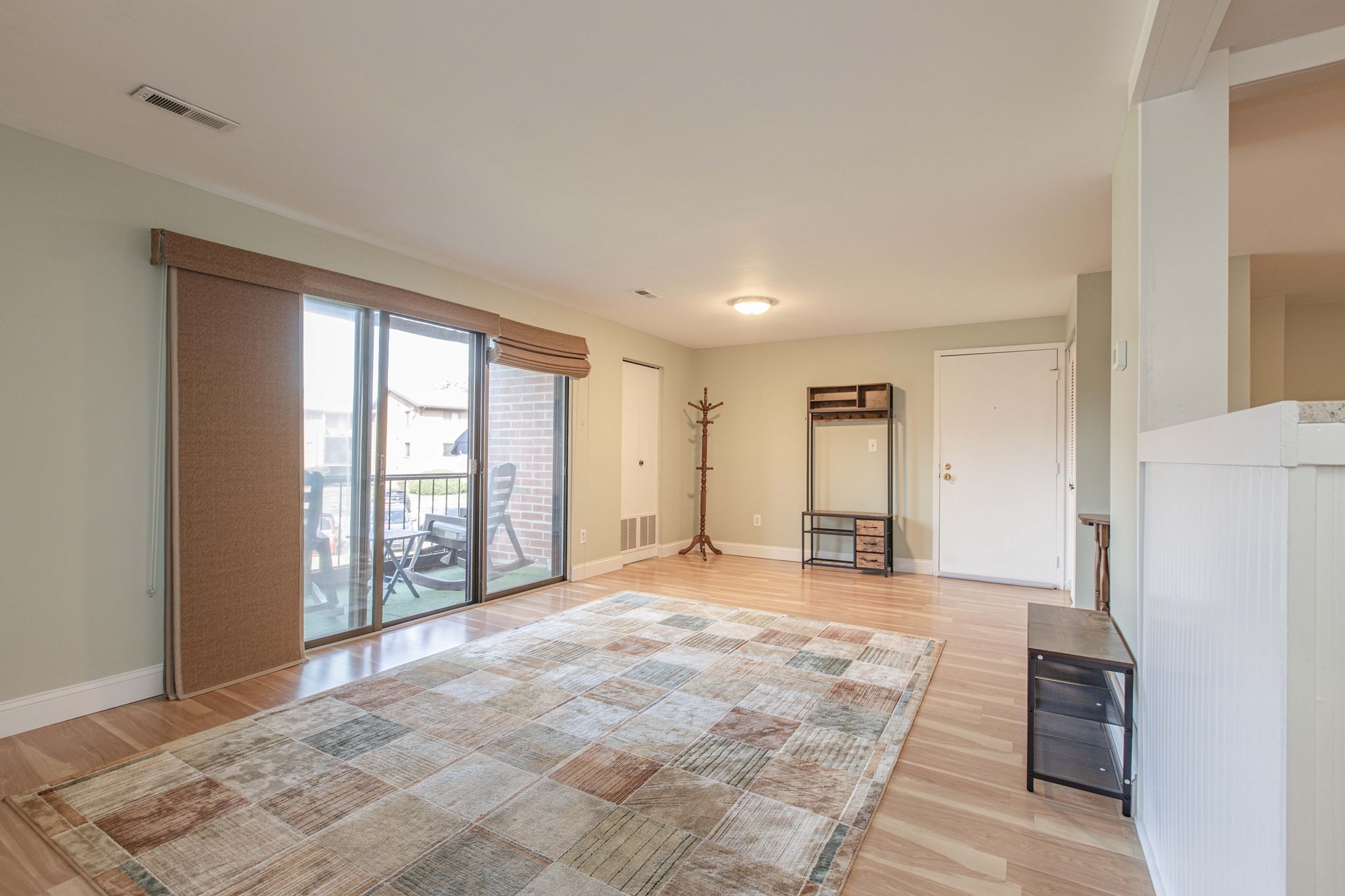 Living room with a patterned rug, light wood floors, and sliding glass doors opening onto a patio.