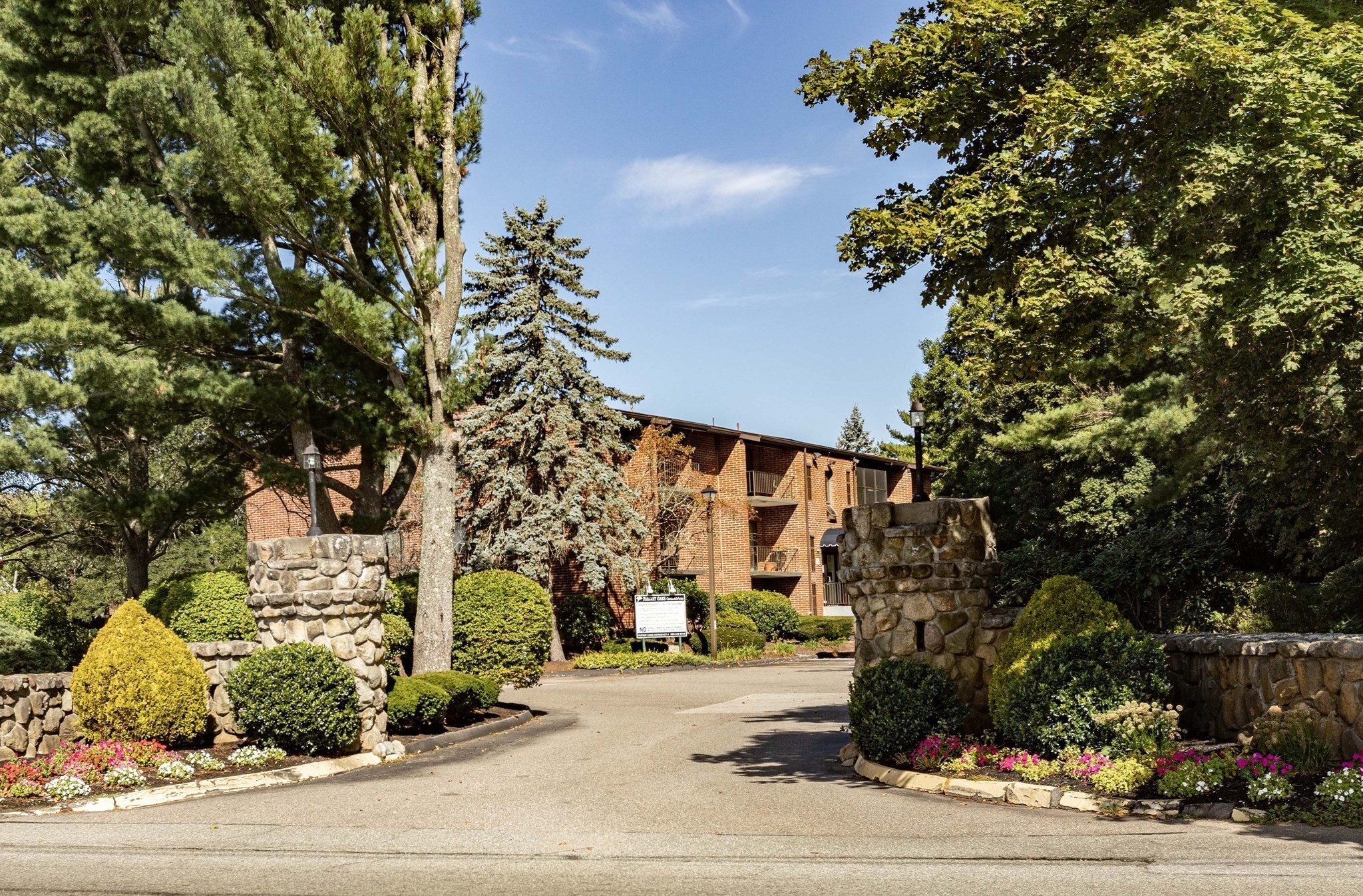 Red-brick apartment building behind stone entrance pillars and landscaped grounds.