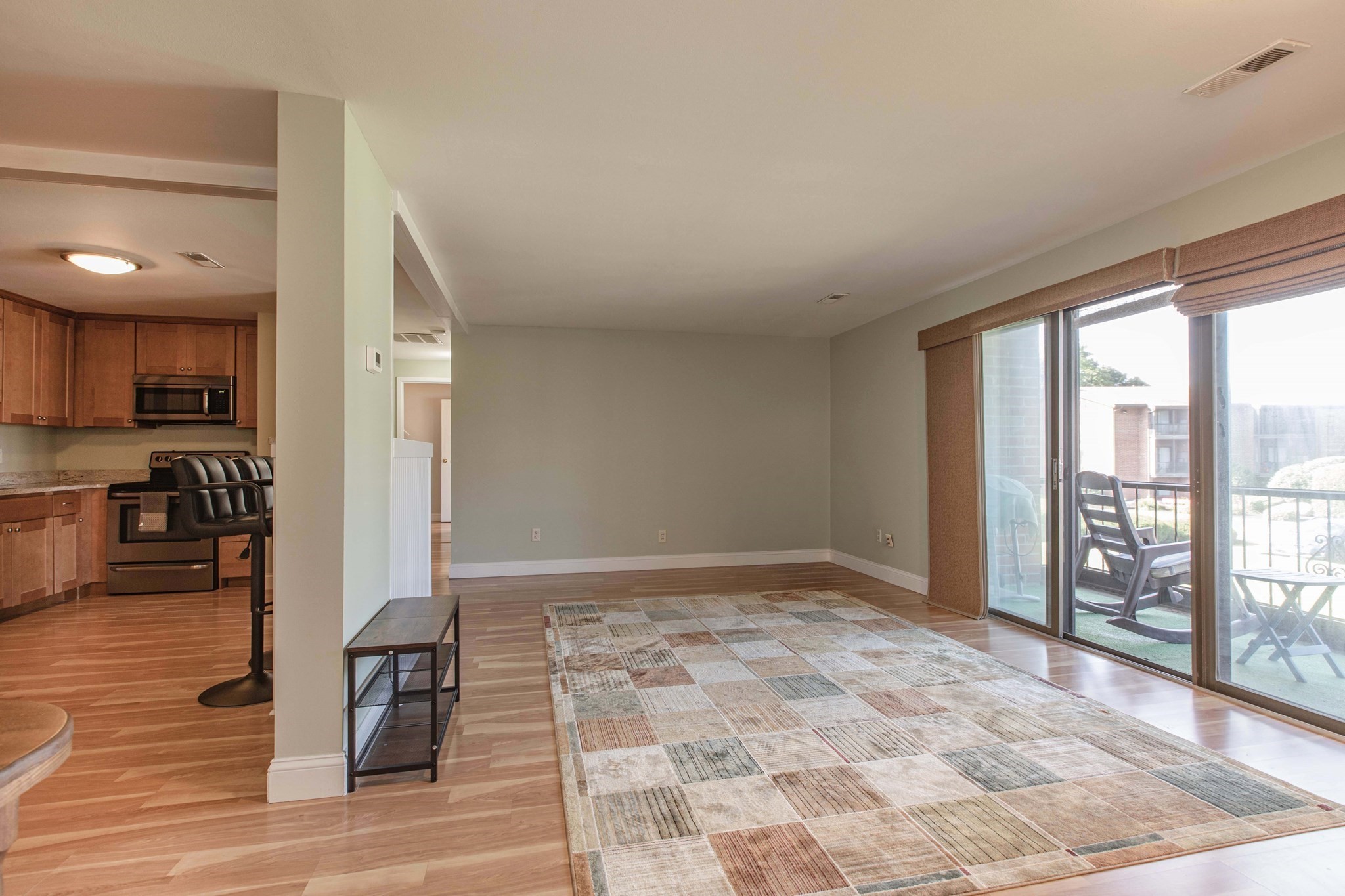 Living area with a patchwork rug, open kitchen, and sliding doors to a balcony.