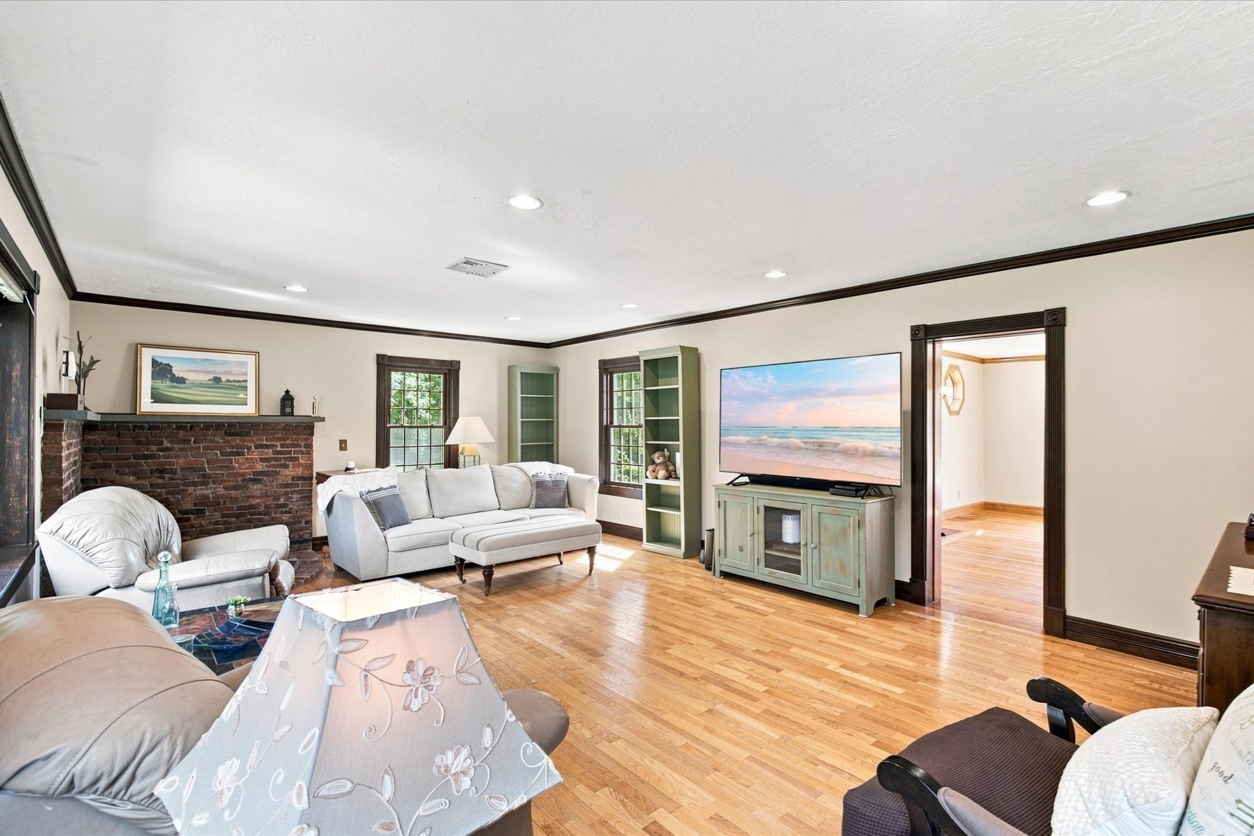Living room with a brick fireplace, hardwood floors, pale seating, and green built-in shelves.