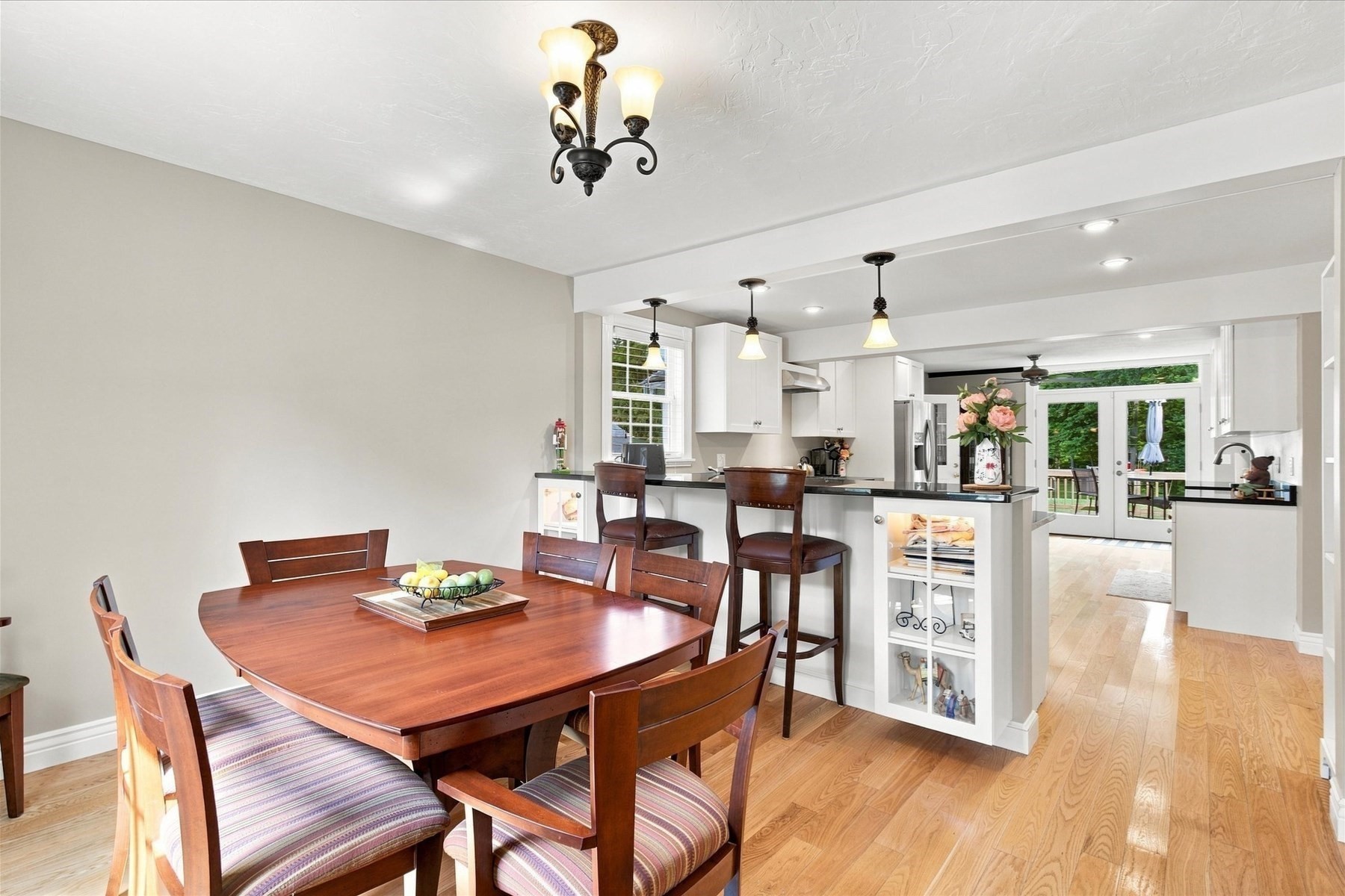 Dining room with a dark wood table opening into a white kitchen and glass doors to the deck.