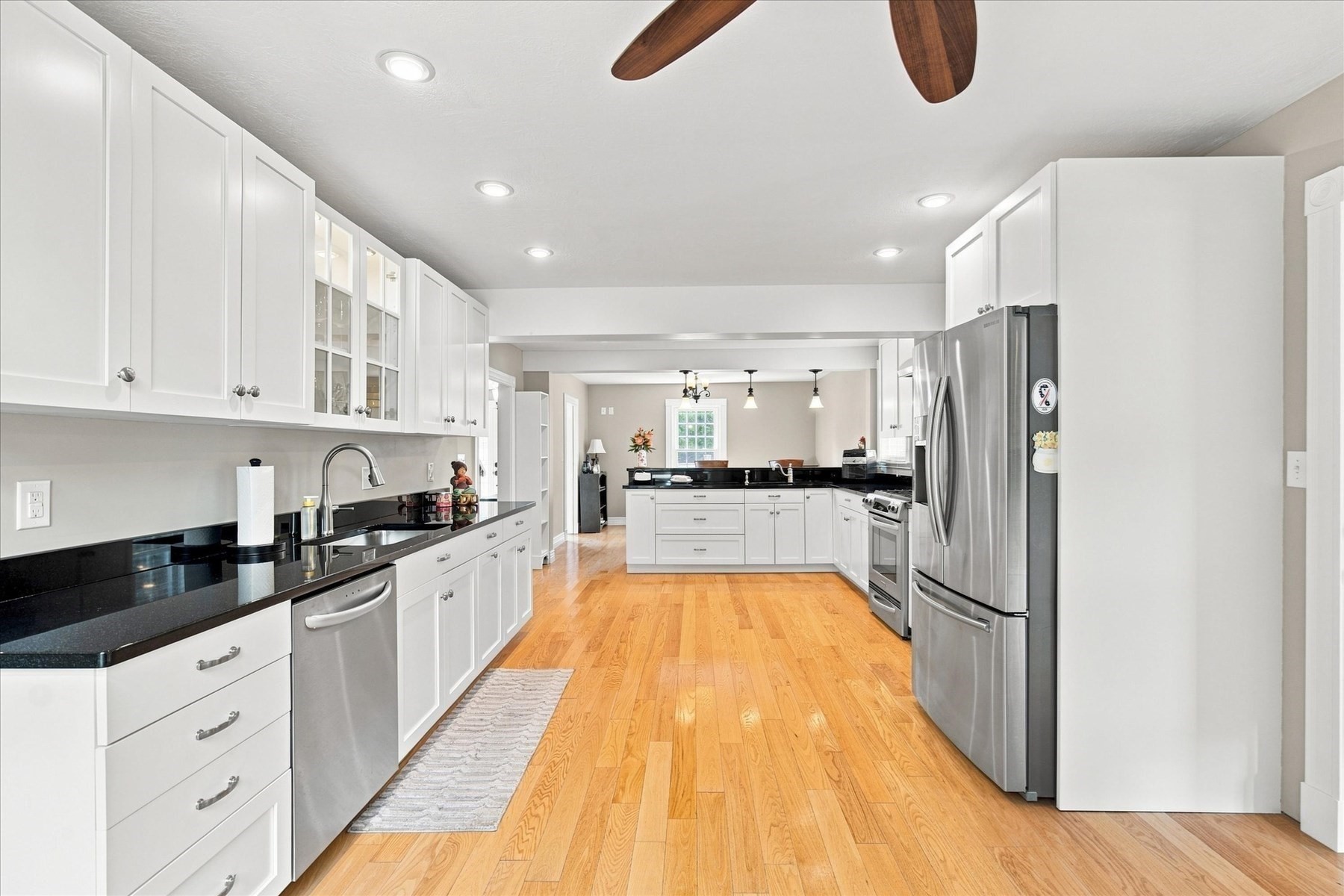 Kitchen with white cabinets, black countertops, stainless steel appliances, and hardwood floors.