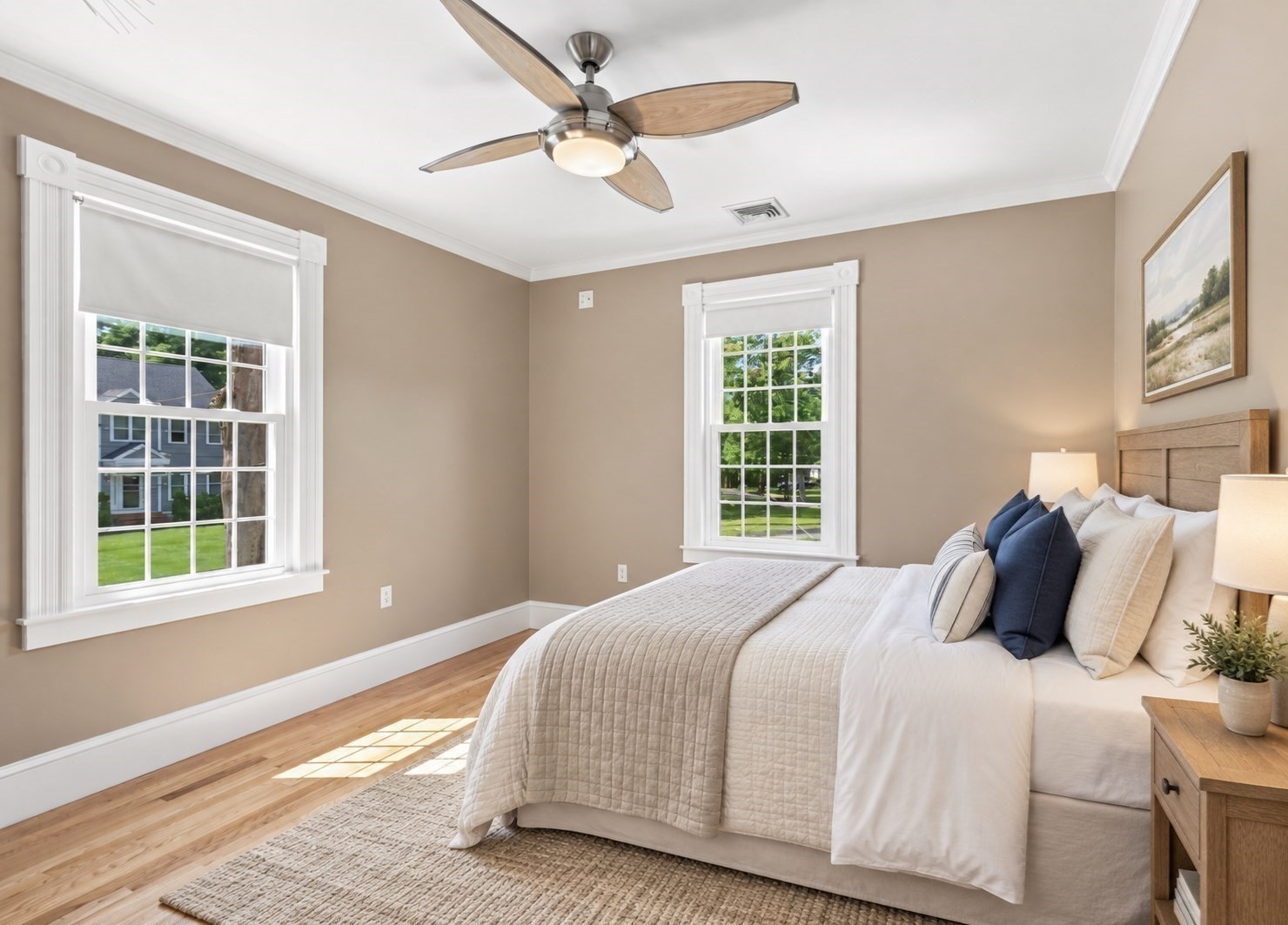 Bedroom with a large bed, two bright windows, a ceiling fan, and hardwood floors.