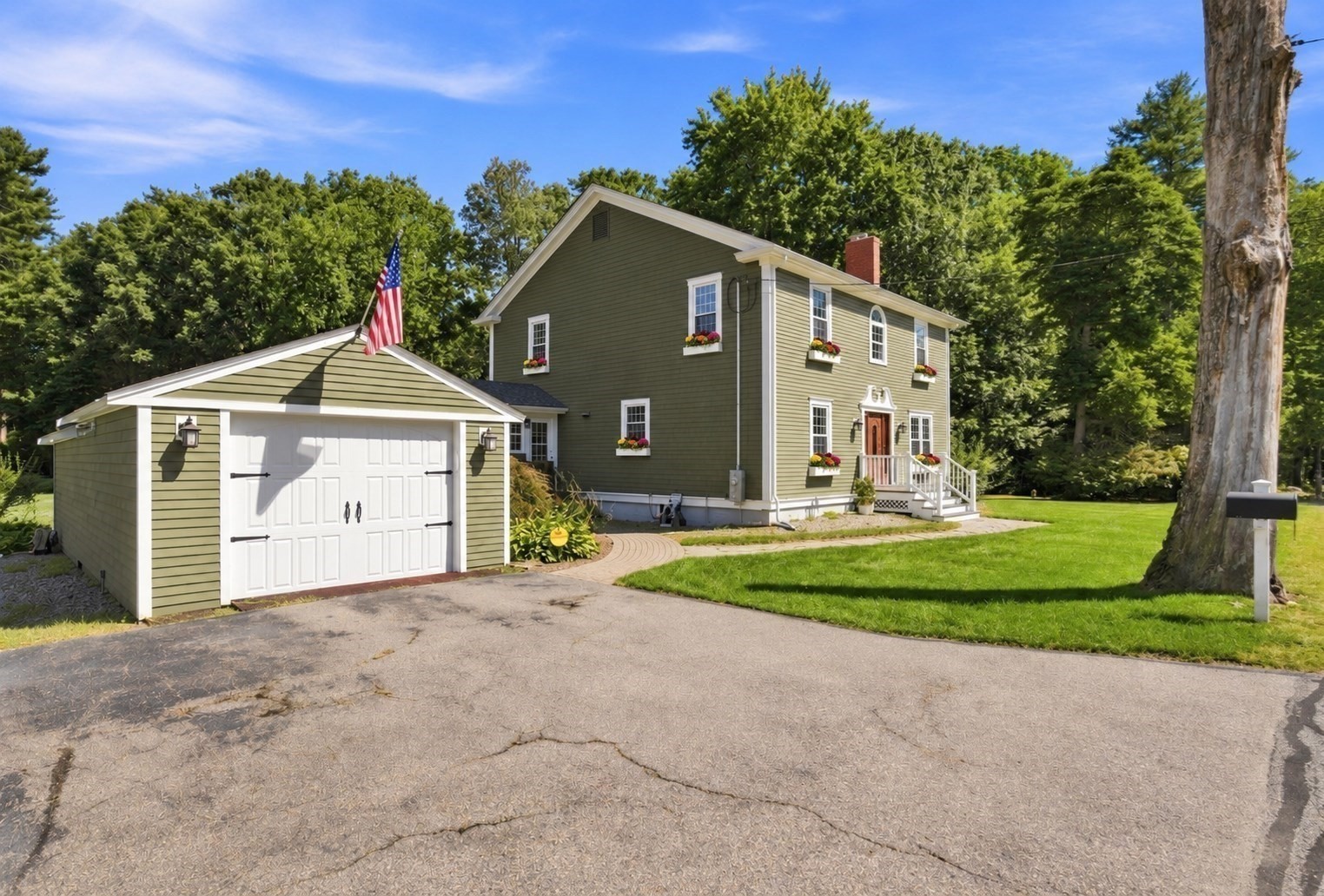 Olive-green two-story house with white trim, flower boxes, attached garage, and an American flag.