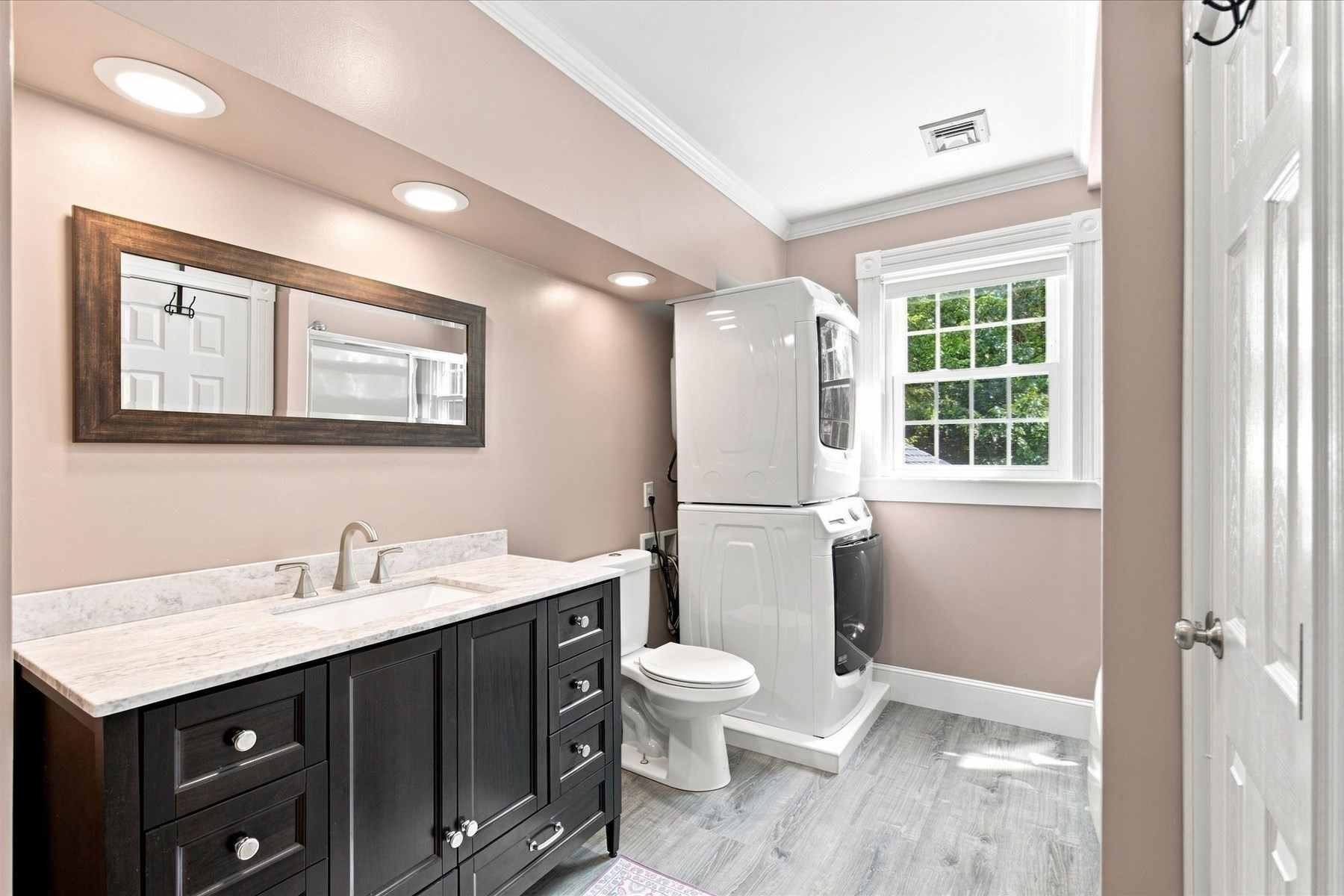 Bathroom with dark wood vanity, toilet, and stacked washer and dryer beside a window.