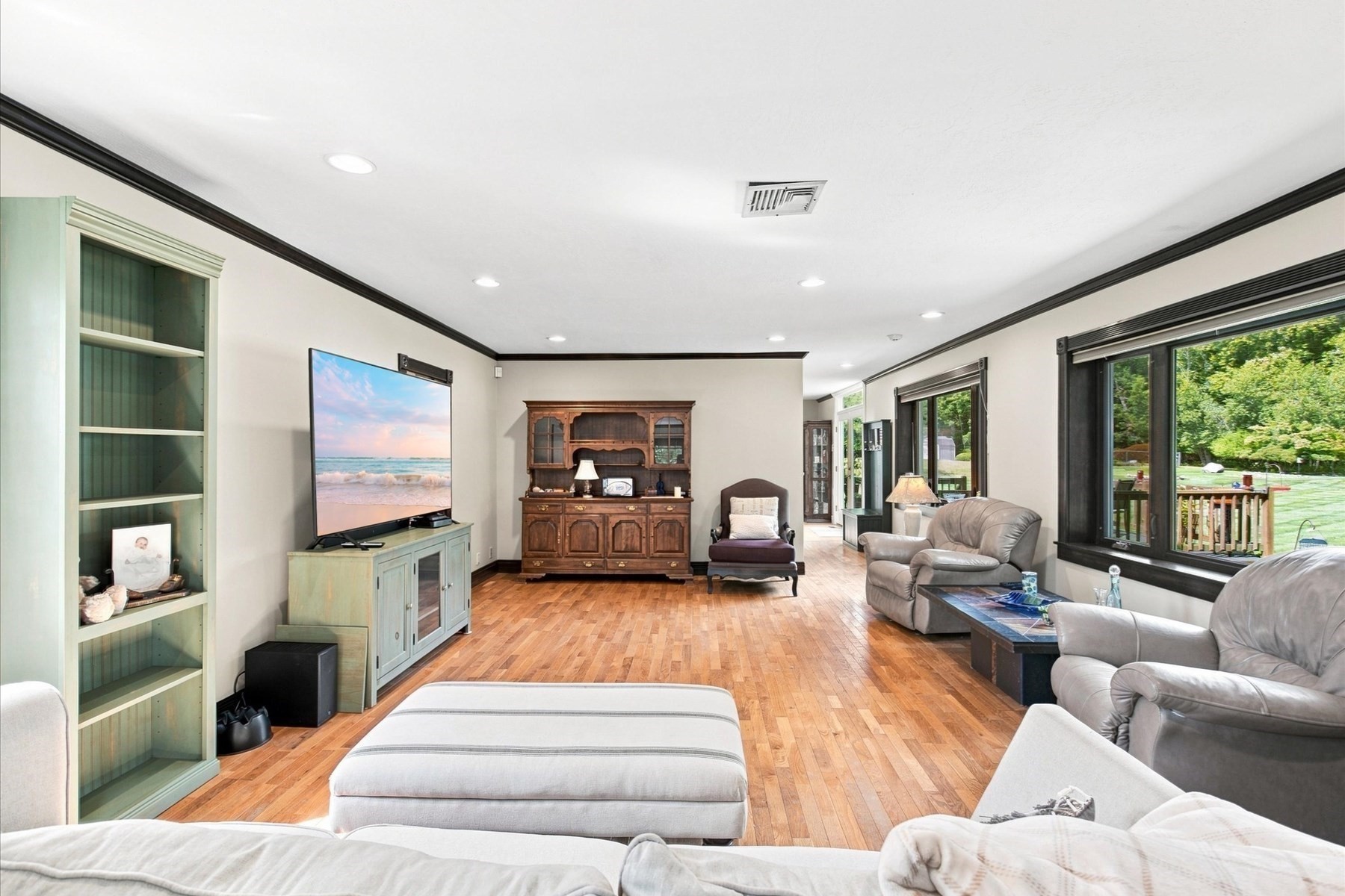 Furnished living room with hardwood floors, built-in shelving, and wide windows overlooking a green yard.