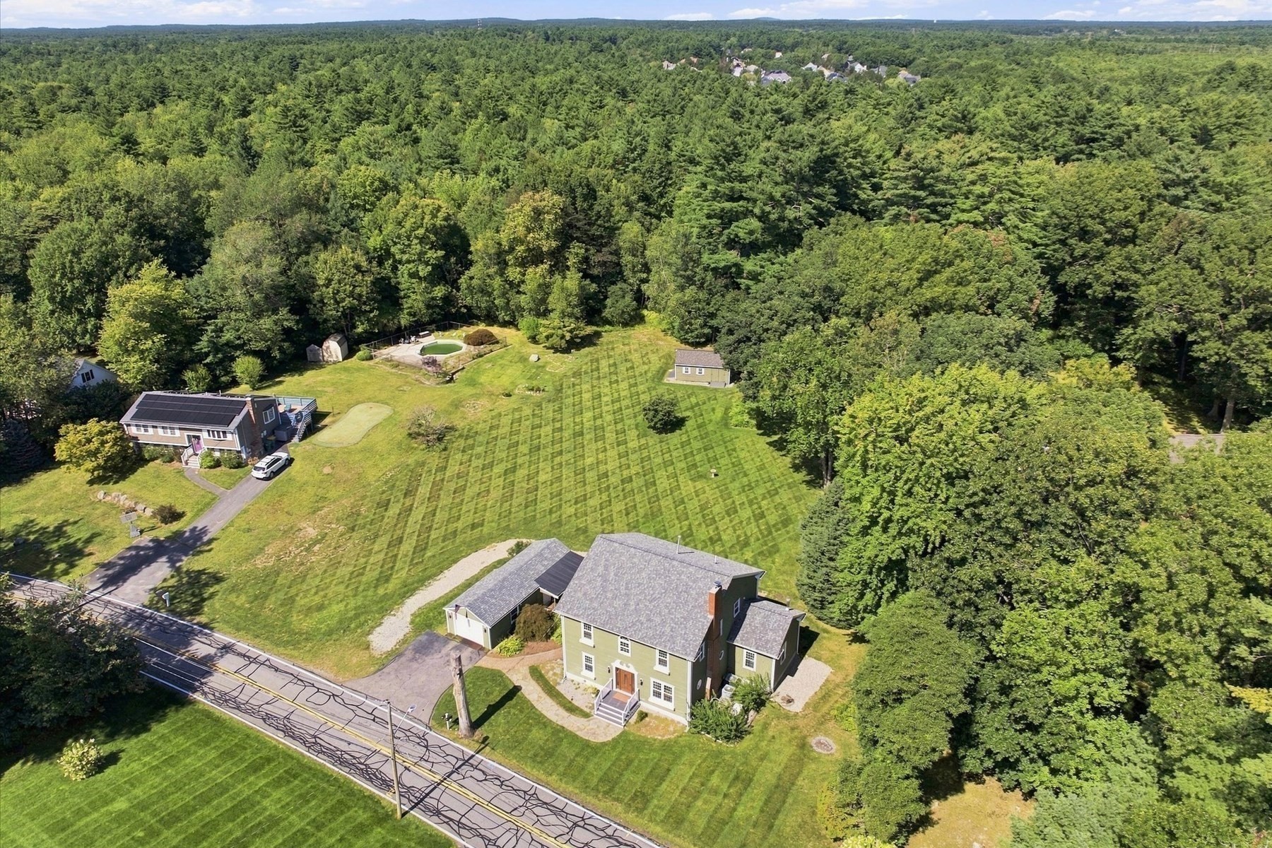 Aerial view of a home, expansive lawn, swimming pool, and surrounding woodland.