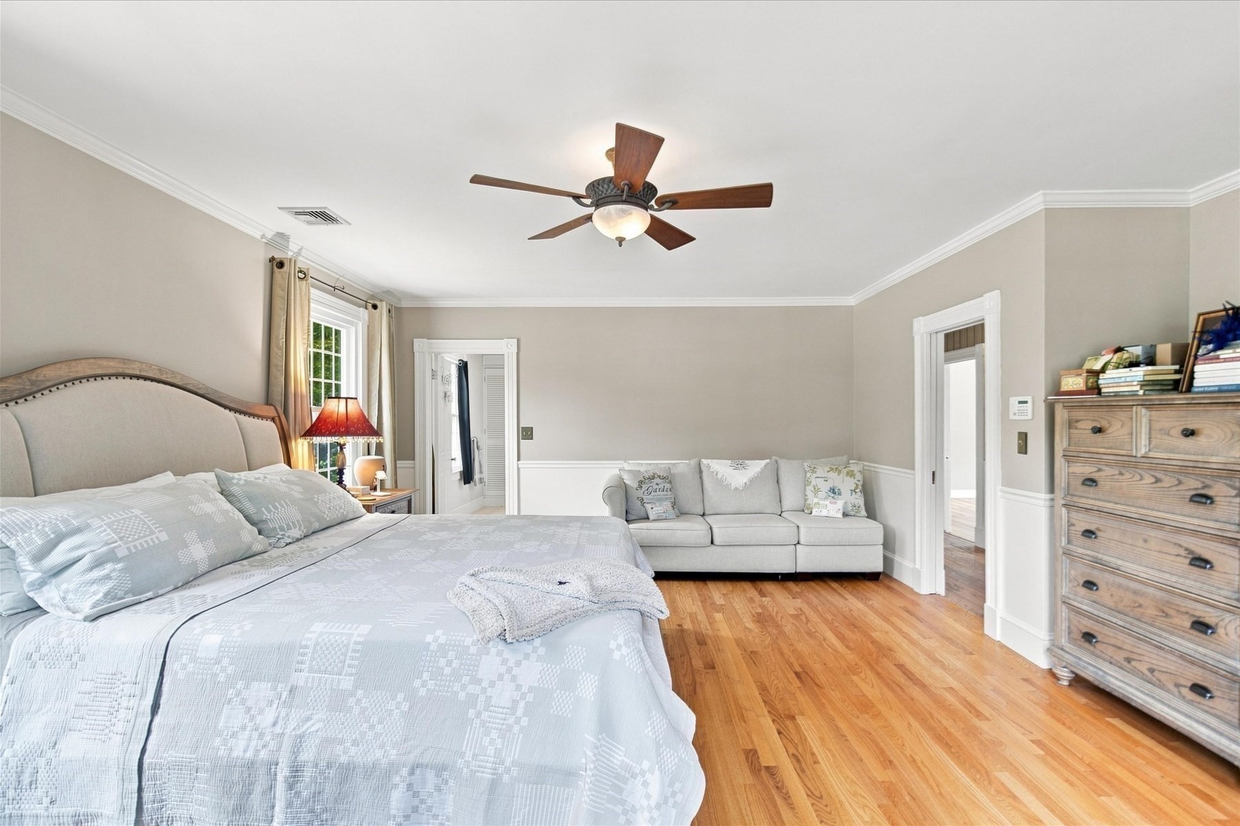 Bedroom with a large bed, sofa seating area, hardwood floors, and ceiling fan.
