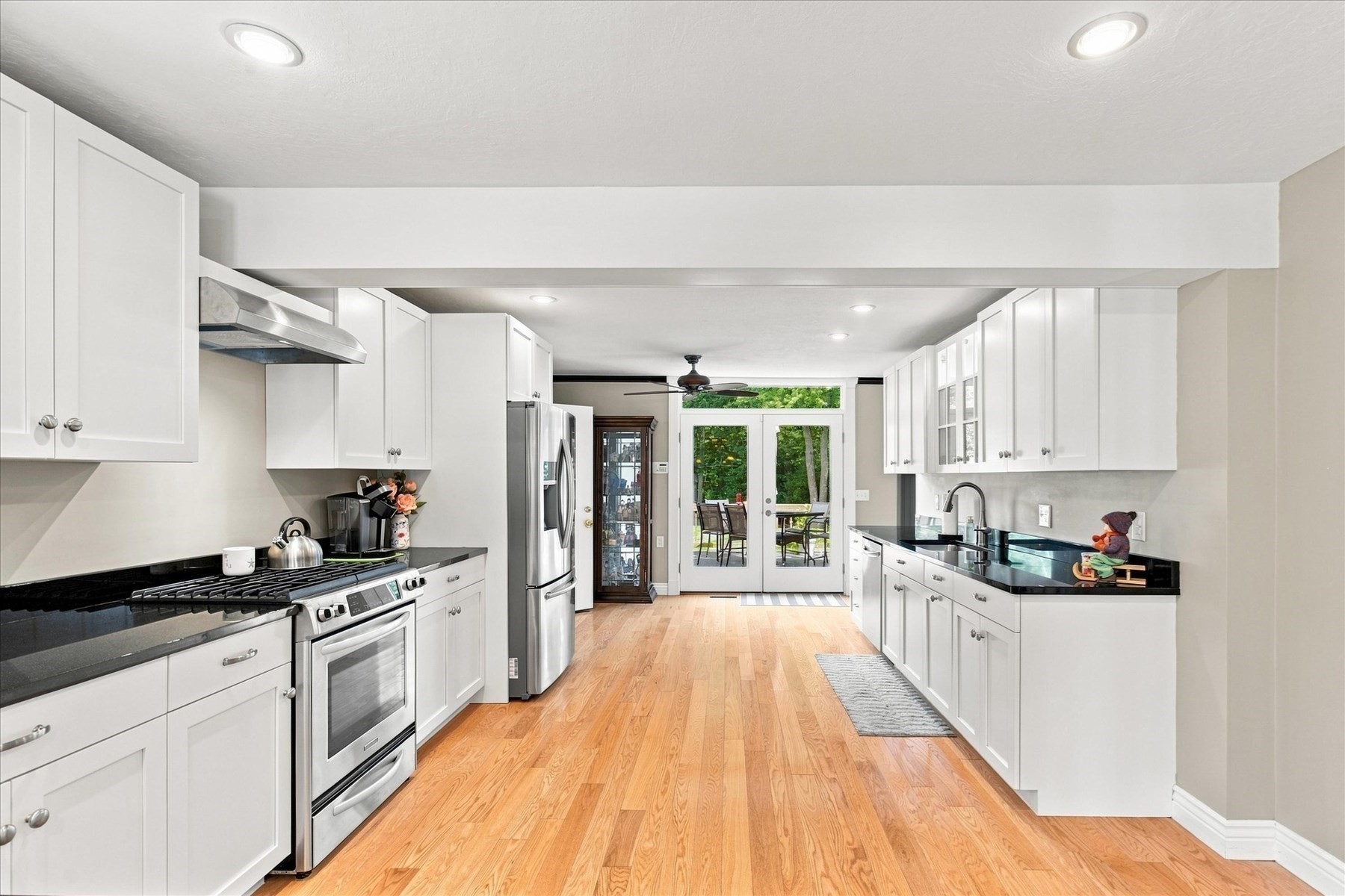 Bright kitchen with white cabinets, black counters, stainless appliances, and glass doors to a tree-lined patio.