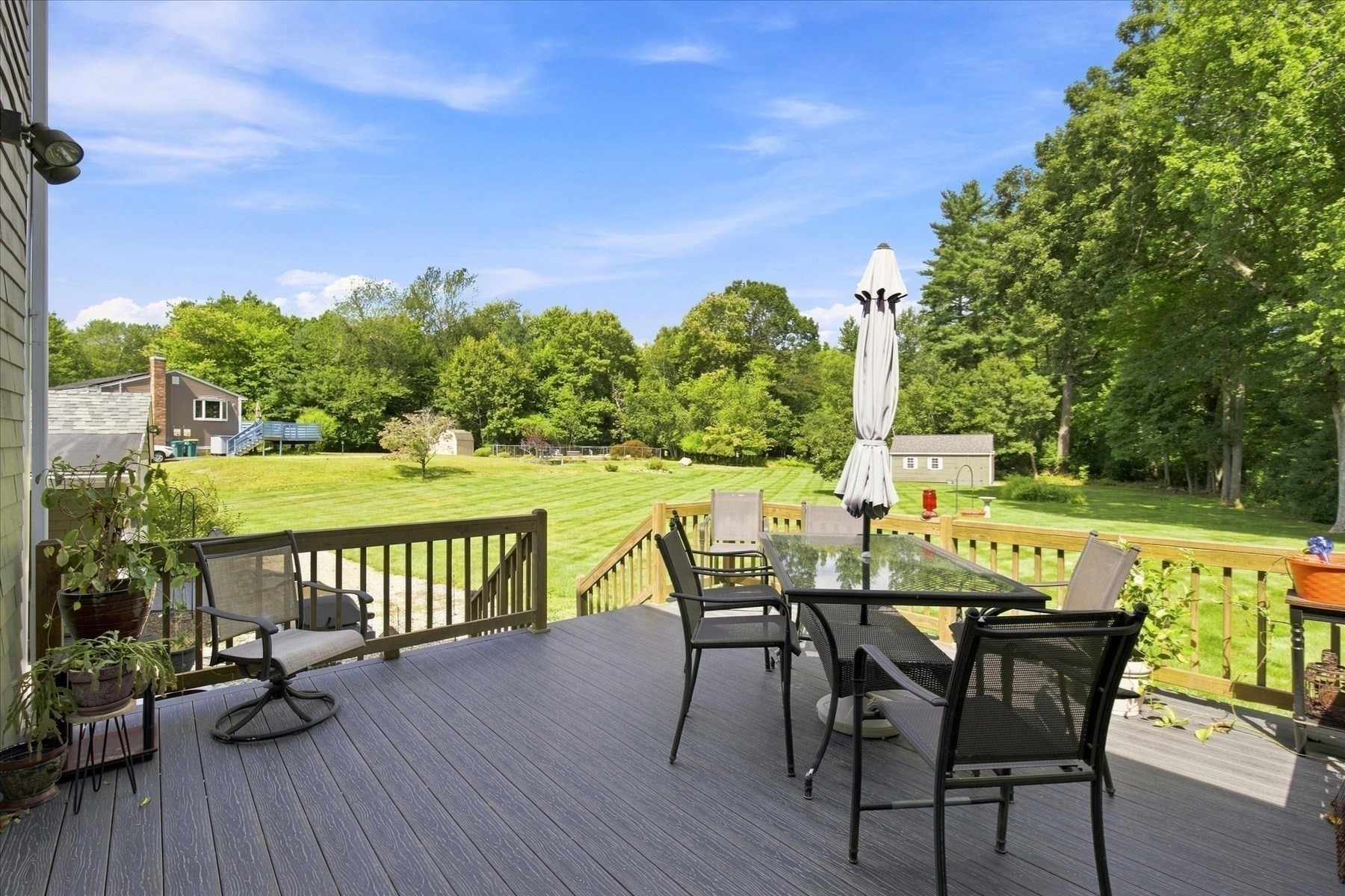 Backyard deck with patio dining set overlooking a broad lawn and mature trees.