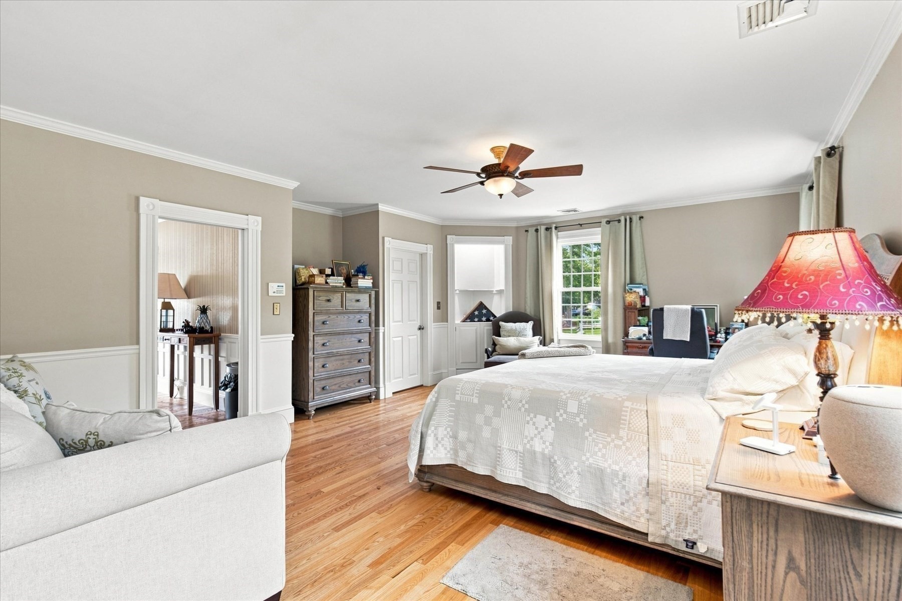 Furnished bedroom with a large bed, hardwood floors, and a sitting area by the windows.