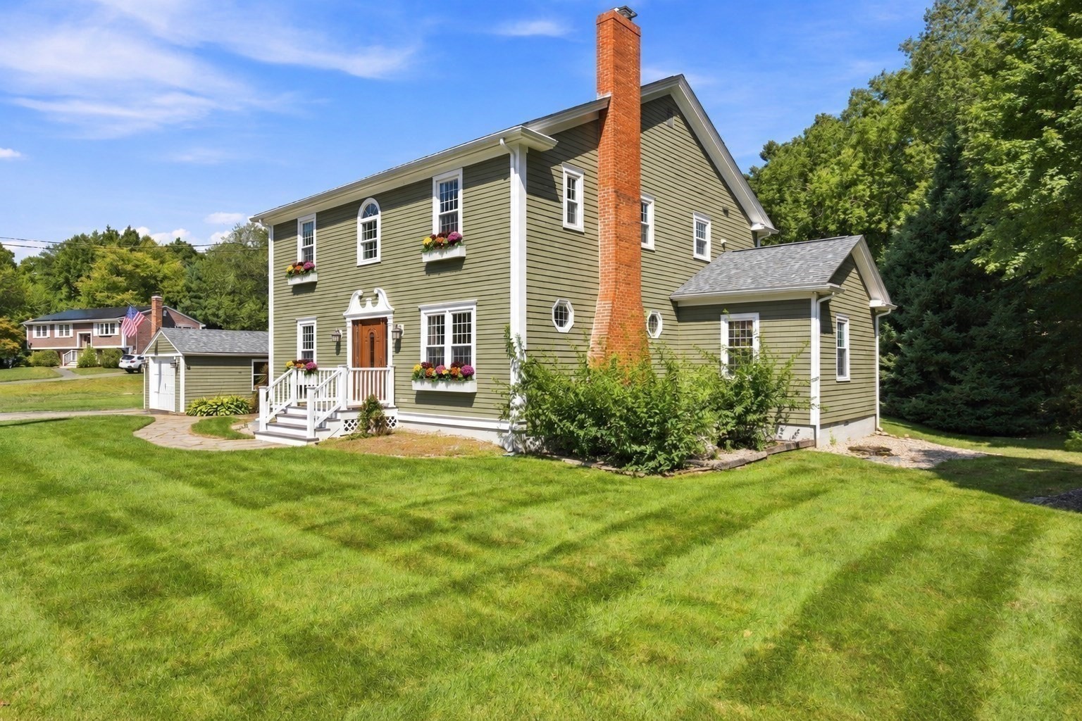 Olive-green two-story house with a tall brick chimney, flower boxes, and a white front porch.
