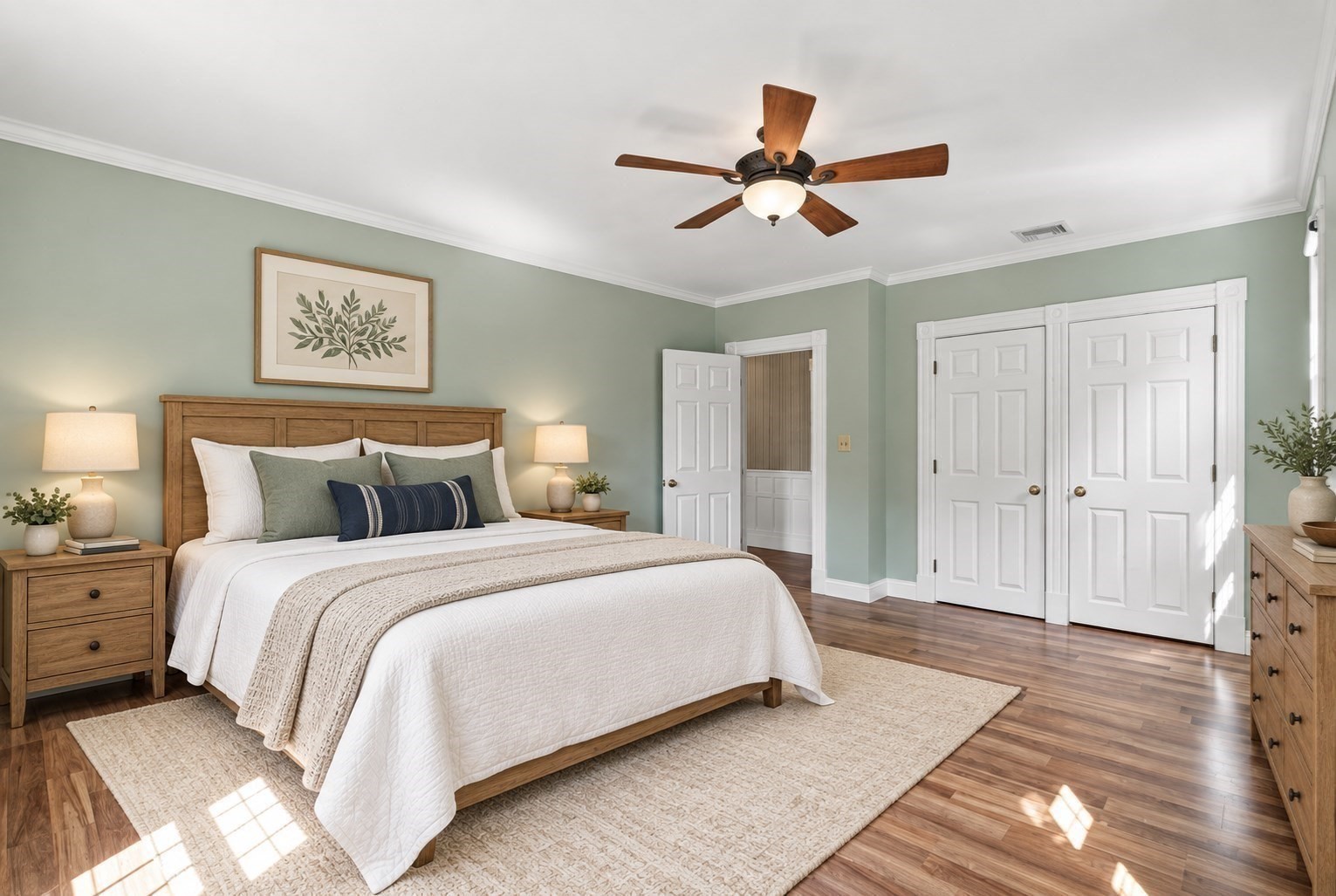 Staged bedroom with a wooden bed, sage-green walls, hardwood floors, and a ceiling fan.