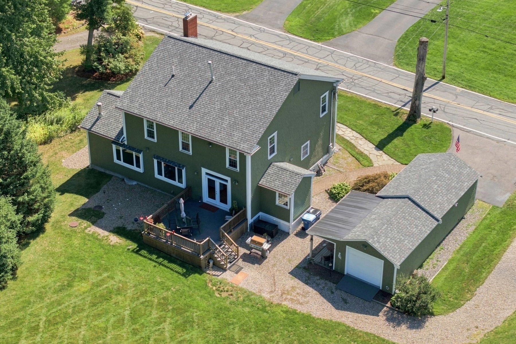 Green two-story house with a rear deck and detached garage, viewed from above.