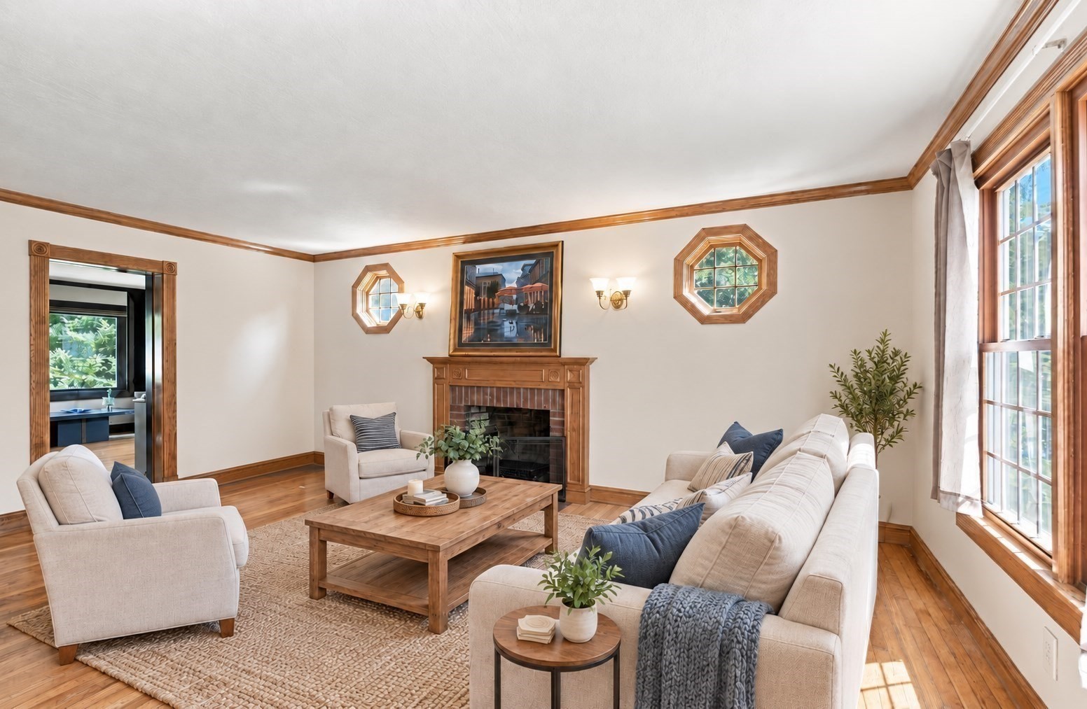 Living room with a wood-trimmed fireplace, cream seating, and large windows.