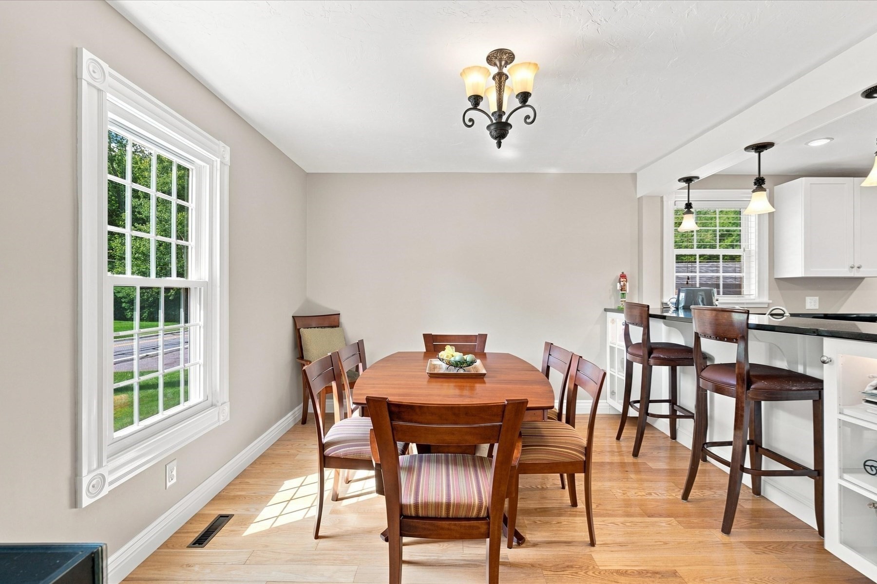 Dining area with a wooden table beside a large window, adjoining a kitchen breakfast bar.