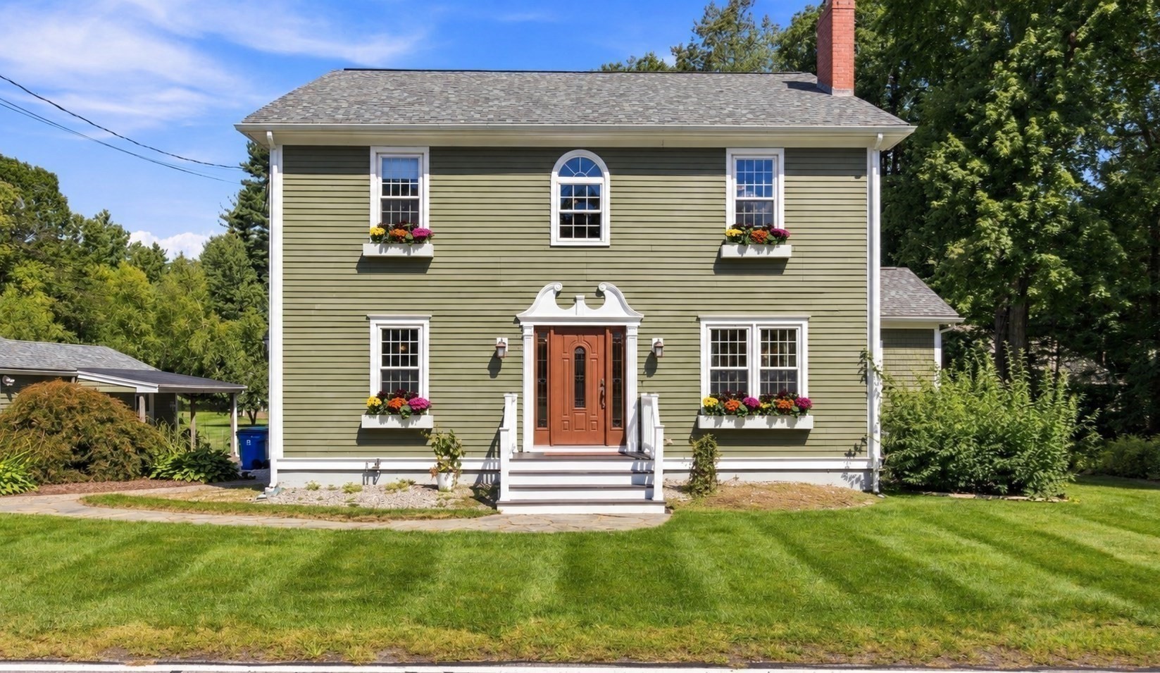 Olive-green two-story house with white trim, colorful flower boxes, and a covered front entry.