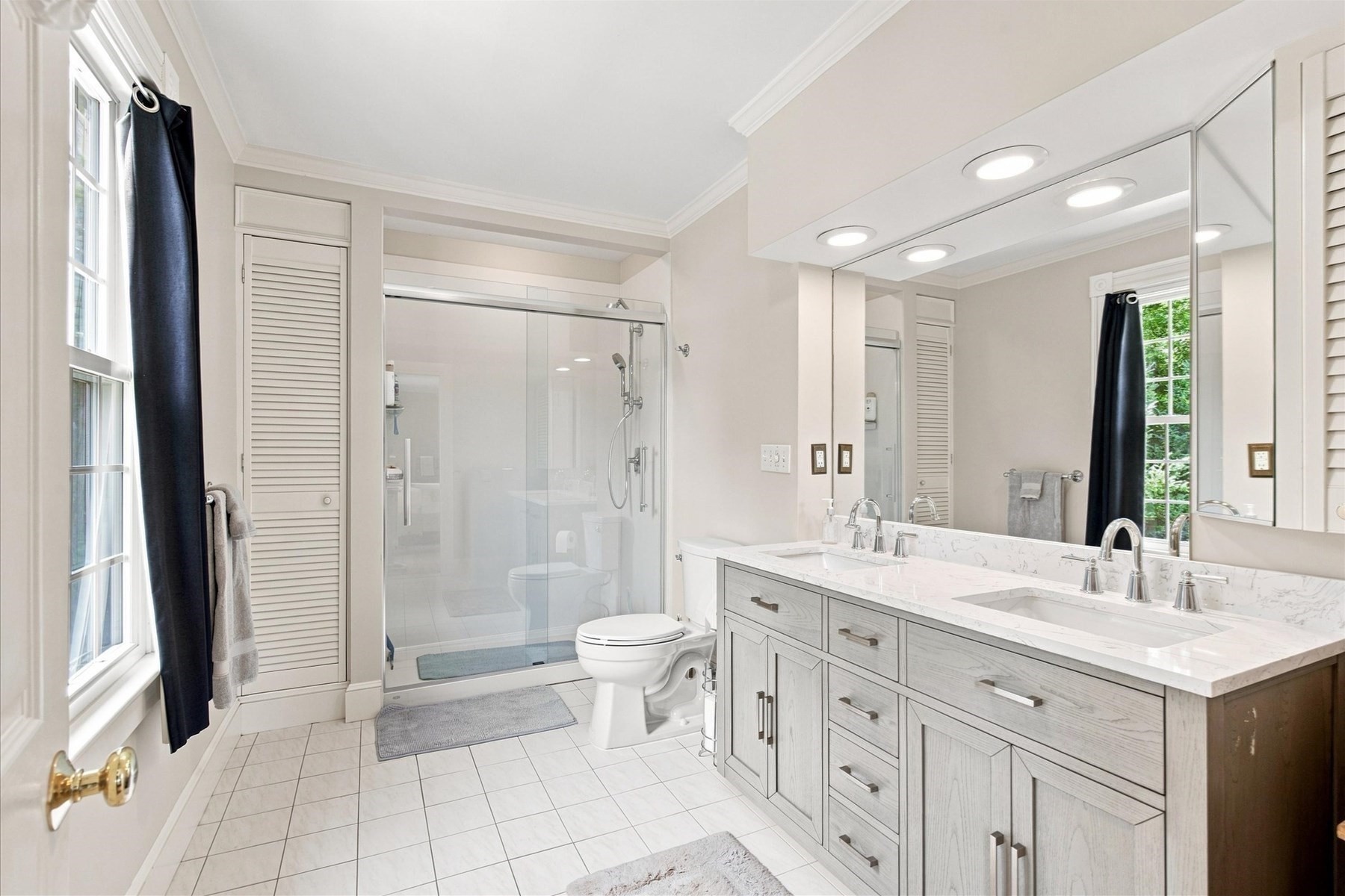 Bright bathroom with a glass shower and long double vanity beneath large mirrors.