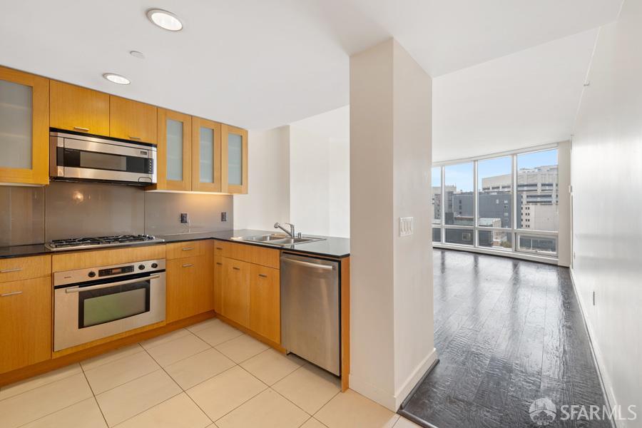 Kitchen with honey-colored cabinets and stainless appliances, opening to a bright living area with city views.