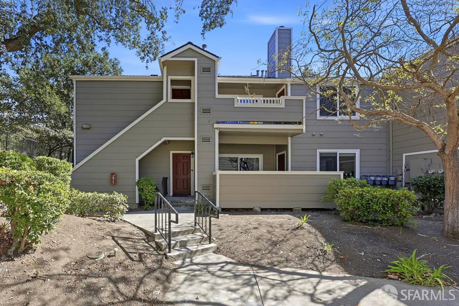 Gray multi-level home with a small balcony, front steps, and trees framing the facade.