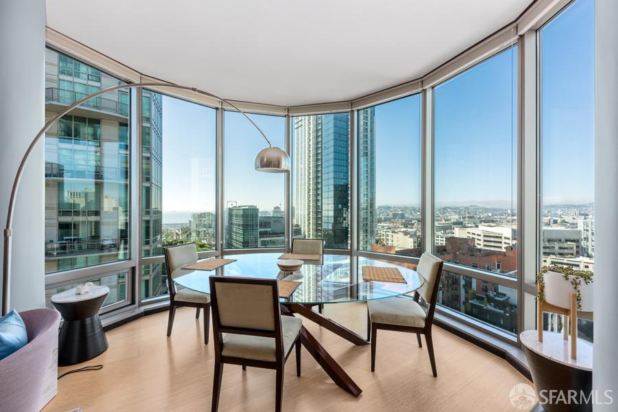 Dining area with a glass-top table and chairs beside floor-to-ceiling windows overlooking the city.