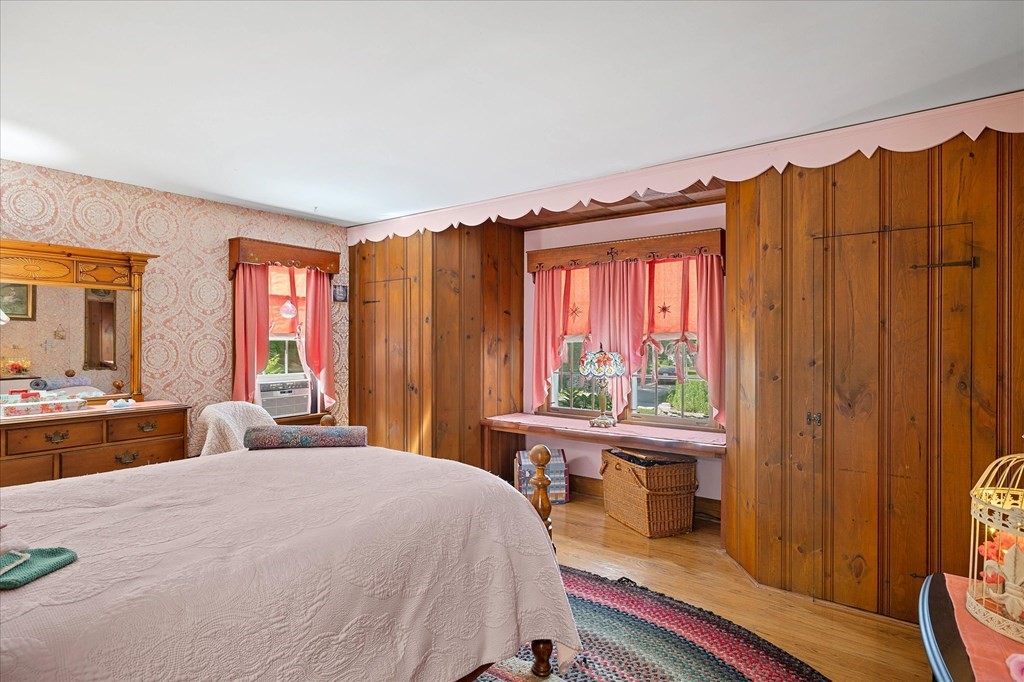 Bedroom with a large bed, wood-paneled walls, built-in closets, and pink curtains.