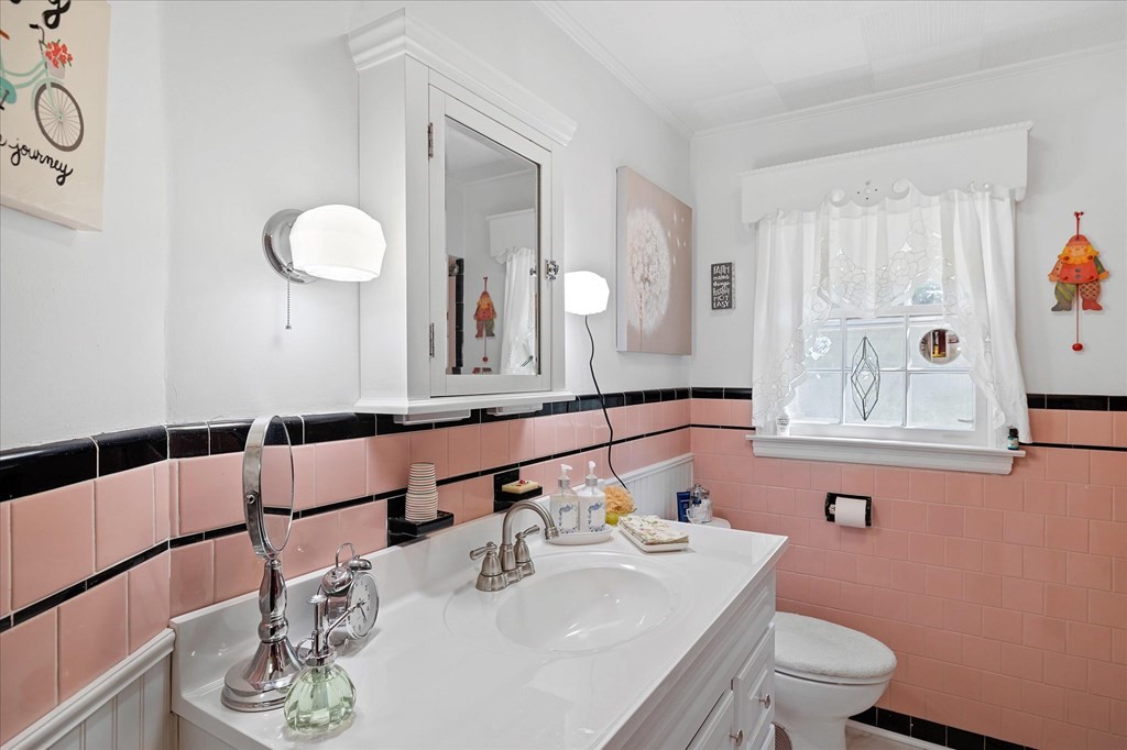 Bathroom with pink tile, black trim, a white vanity, mirrored cabinet, and curtained window.